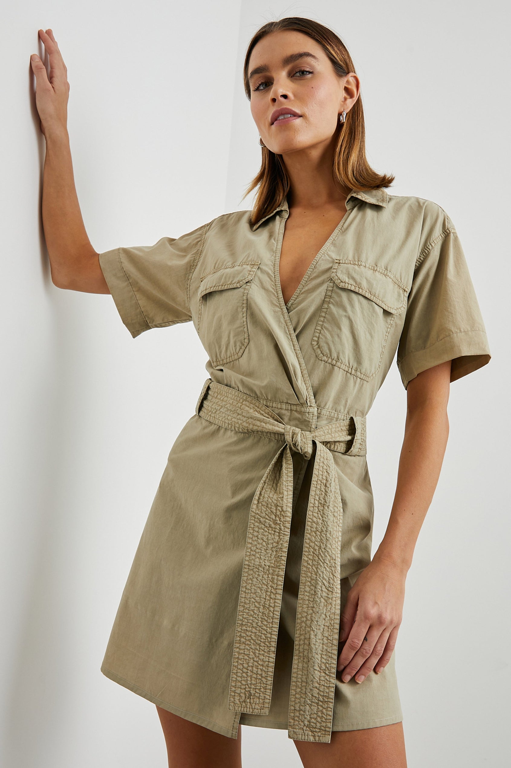 Natalie Short Sleeve Mini Dress with a Deep V Neck, Fabric Tie Belt, Belt Loops, Two Chest Flap Pockets, Buttoned Horizontal Flap on the Back and a Collar in Olive Colorway - Front View Featured on Model 