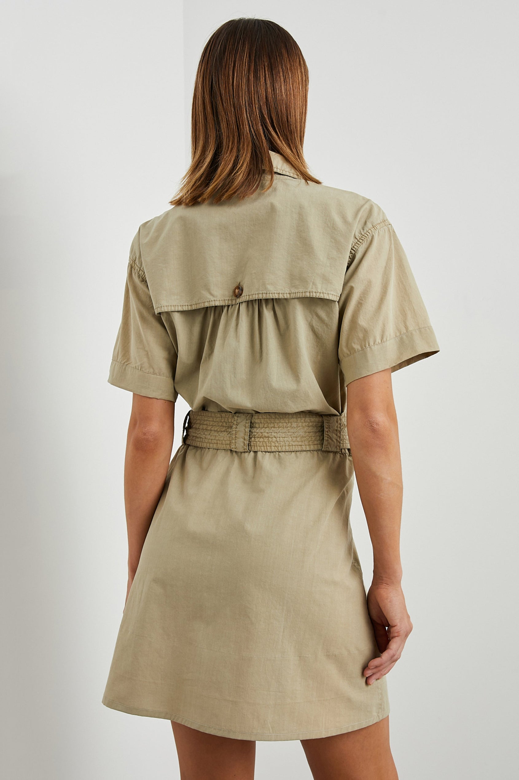 Natalie Short Sleeve Mini Dress with a Deep V Neck, Fabric Tie Belt, Belt Loops, Two Chest Flap Pockets, Buttoned Horizontal Flap on the Back and a Collar in Olive Colorway - Back View Featured on Model 