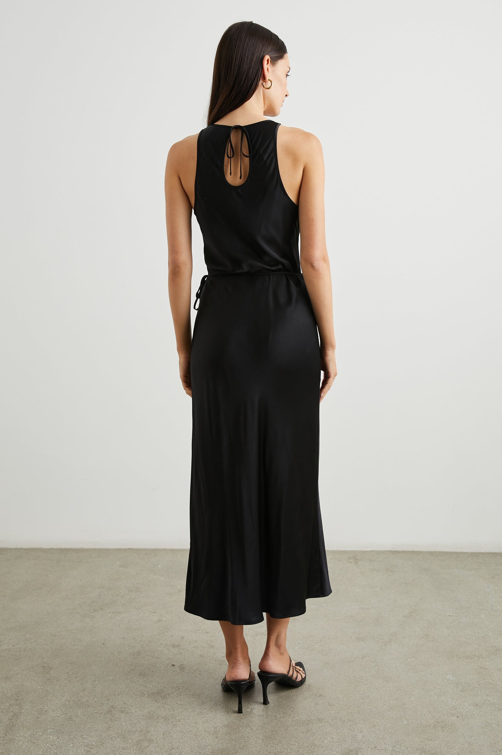 Navi Sleeveless Midi Dress with a Halter Neckline with a Back Tie Keyhole, and a Wrap Skirt with a Side Tie Closure in Black Colorway - Back Full Body View Featured on Model  
