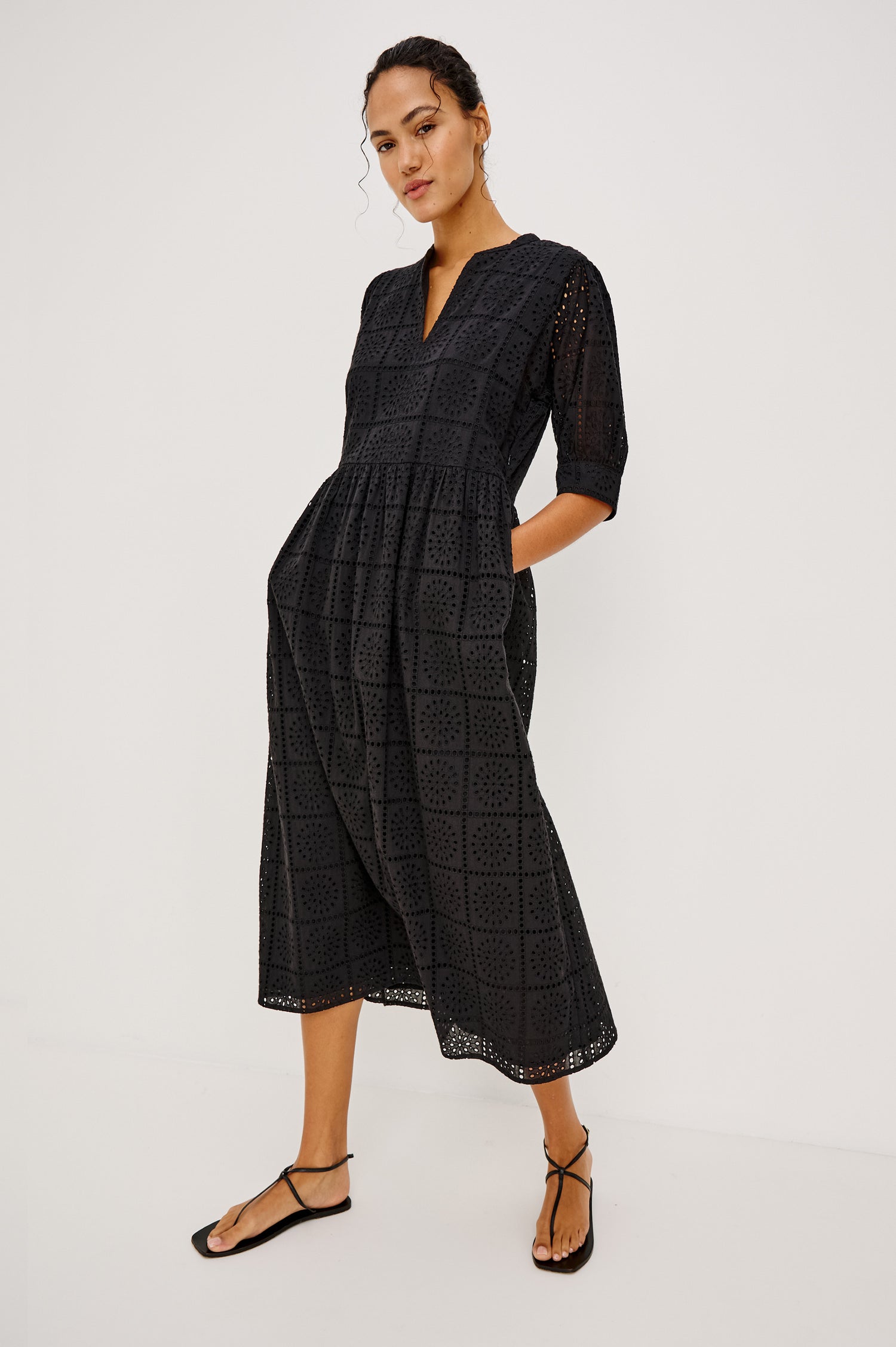 Nella Smock Maxi Dress in Cotton With Grid Eyelet Embroidery Lined Body Split Band V-Neckline Drop Waist Gathered Skirt and Short Puff Sleeves With Fitted Cuffs in Black Colorway - Full Body Front View Featured on Model