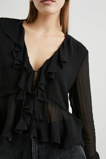 Nicoletta Long-Sleeve Semi-Sheer Top with Deep V Neck, Front Tie Closure, and Ruffled Trim in Black Colorway - Front View Featured on Model