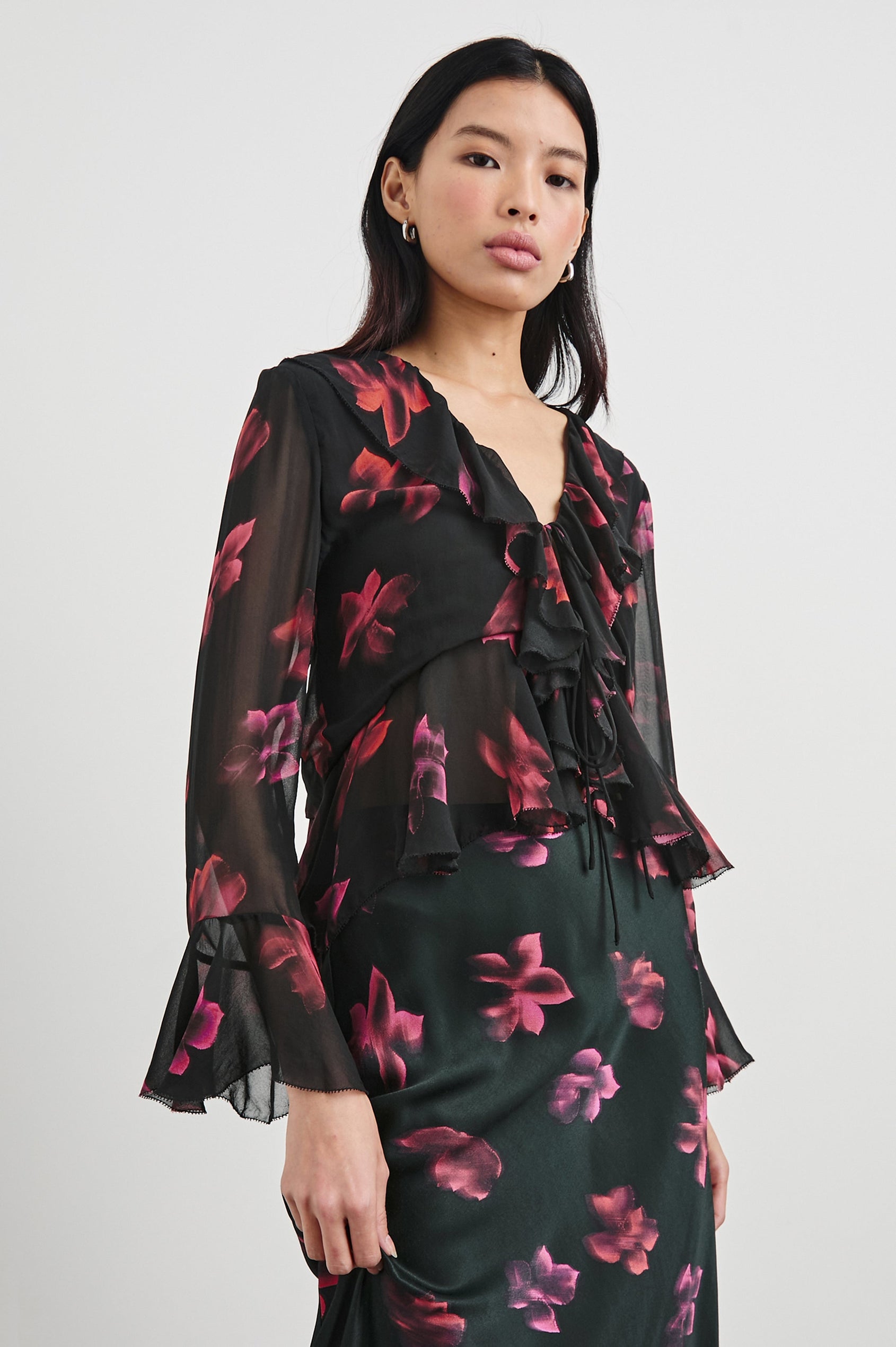 Nicoletta Long-Sleeve Semi-Sheer Top with Deep V Neck, Front Tie Closure, and Ruffled Trim in Dark Azalea Colorway, Flowers in pinks and purple on Black - Front View Featured on Model
