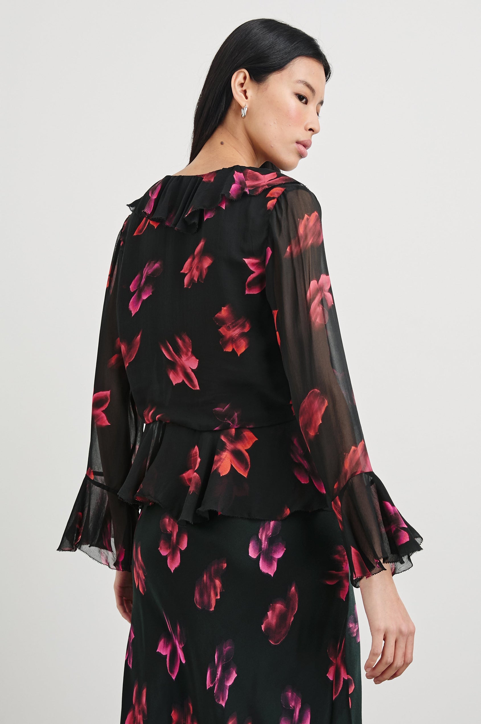 Nicoletta Long-Sleeve Semi-Sheer Top with Deep V Neck, Front Tie Closure, and Ruffled Trim in Dark Azalea Colorway, Flowers in pinks and purple on Black - Back View Featured on Model