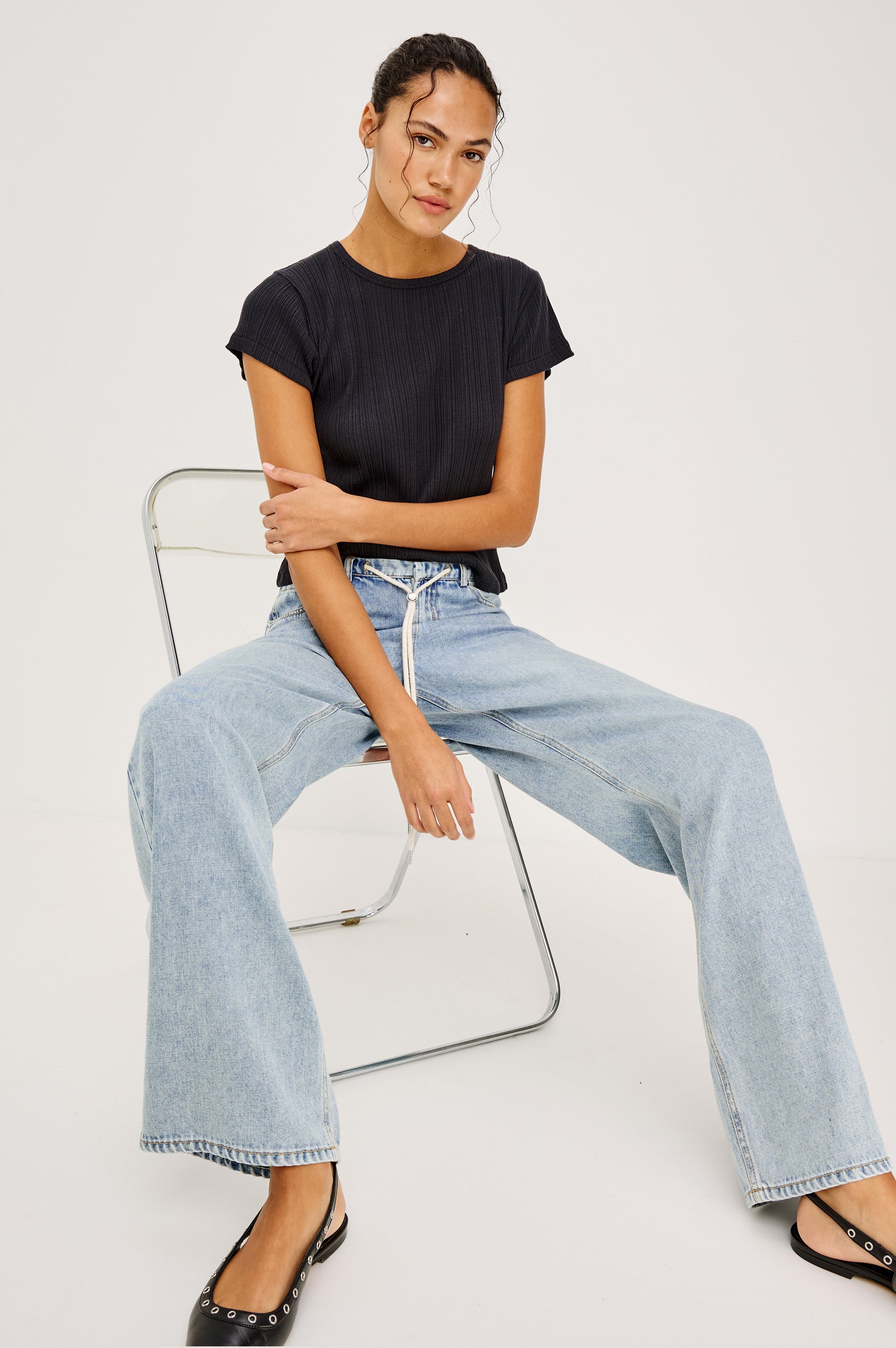Normandie Pant in Cotton Lyocell Denim With Low-Slung Fit, Adjustable Toggle Drawstring Waist Ties, 5-Pockets, and Loose Fit in Sun Kissed Blue Colorway - Full Body View Featured on Model Sitting