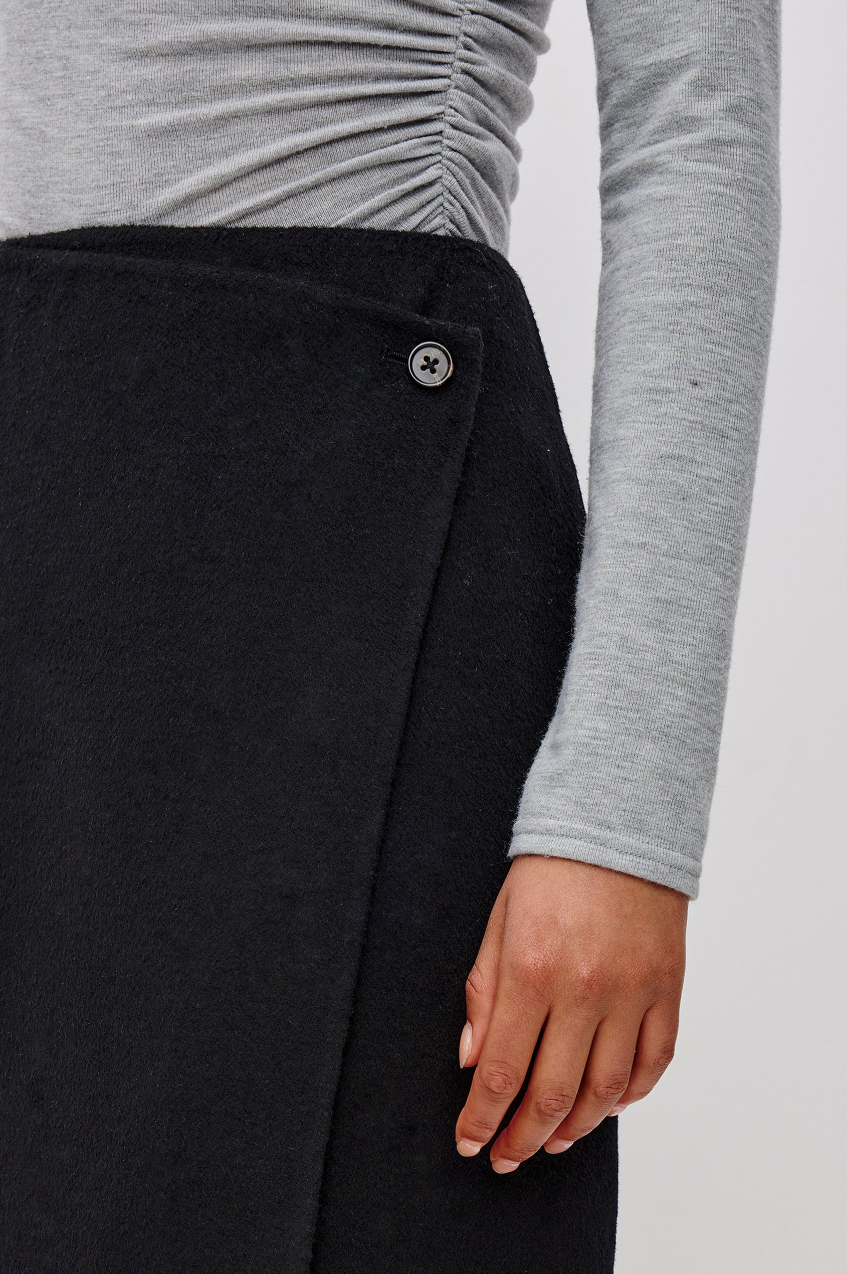 Odette Midi Skirt in Wool Blend With Wrap Design, Hidden Side Button Closure, and Fringe Hem in Black Colorway - Lower Body Front Close Up View Featured on Model