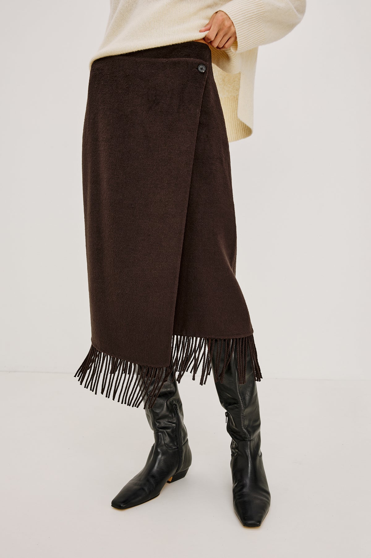 Odette Midi Skirt in Wool Blend With Wrap Design, Hidden Side Button Closure, and Fringe Hem in Chocolate Colorway - Lower Body Front View Featured on Model
