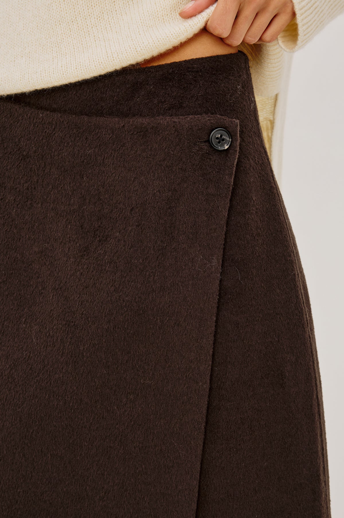 Odette Midi Skirt in Wool Blend With Wrap Design, Hidden Side Button Closure, and Fringe Hem in Chocolate Colorway - Lower Body Front Close Up View Featured on Model