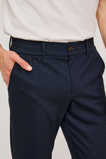 The Olivier is a trouser with a front zip fly, belt loops, side pockets, and pintuck detailing in Navy colorway. Front detail view featured on model.