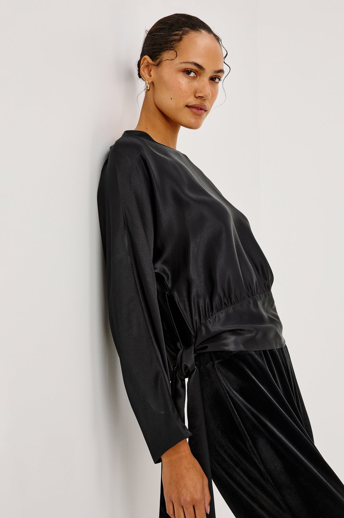 Opal Long-Sleeve Top in Luxe Satin With a Self Tie Hem in Black Colorway - Side Crop View Featured on Model.