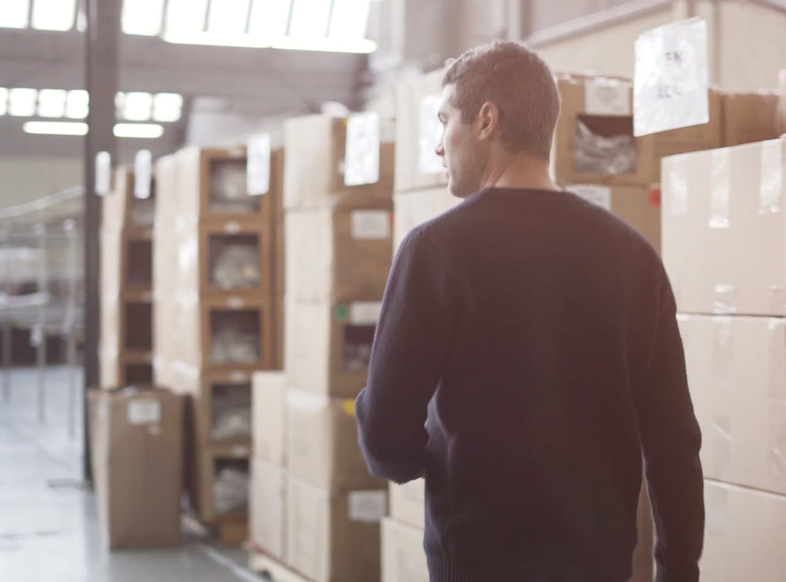 MAN WALKING THROUGH A WAREHOUSE SURROUNDED BY STACKED CARDBOARD BOXES