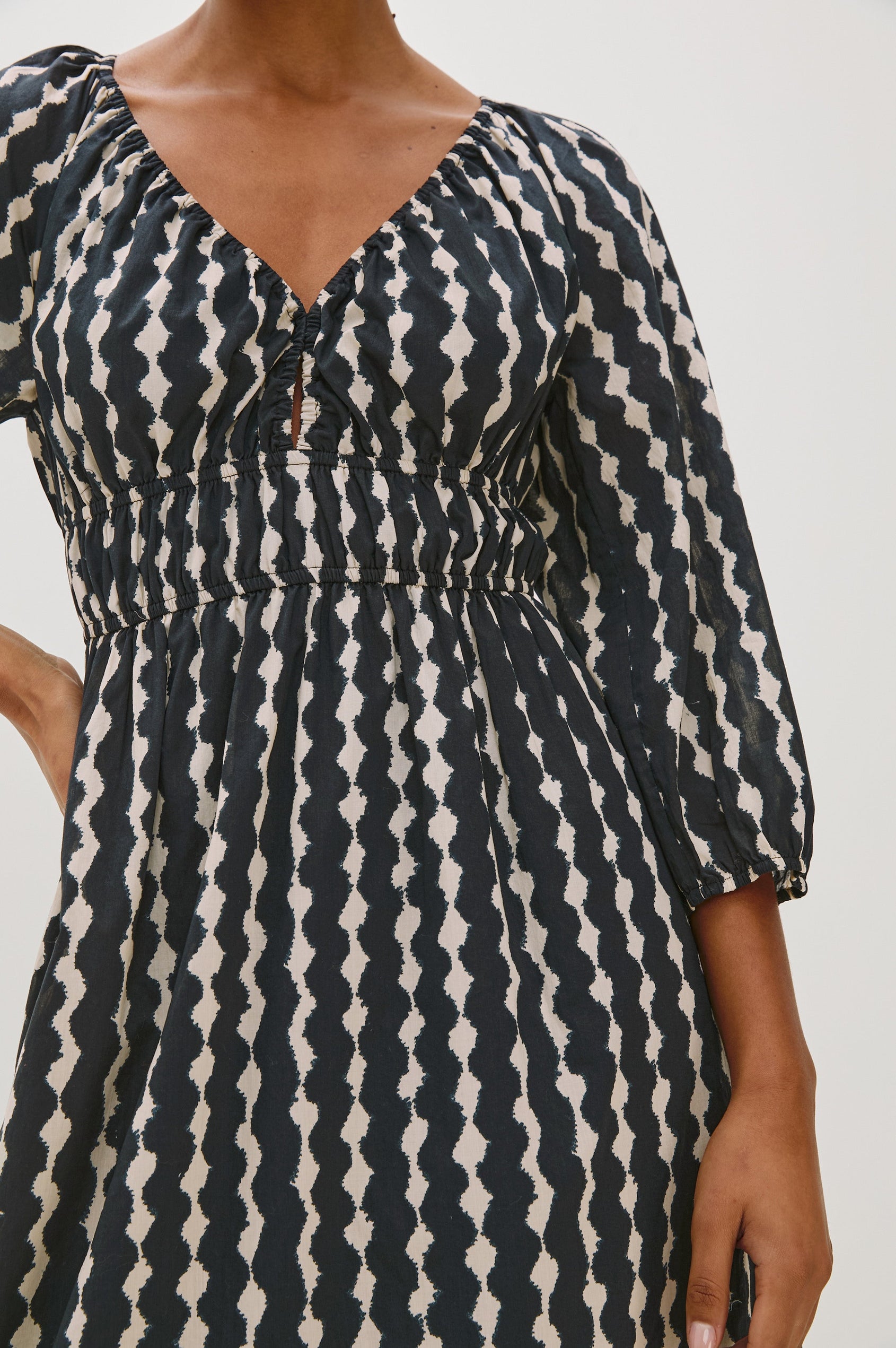 Paio midi dress with a fitted bodice, three quarter sleeves with a slight puff effect, flowing skirt, and eyelet closures at the chest in Painted Noir colorway - close up of details on model