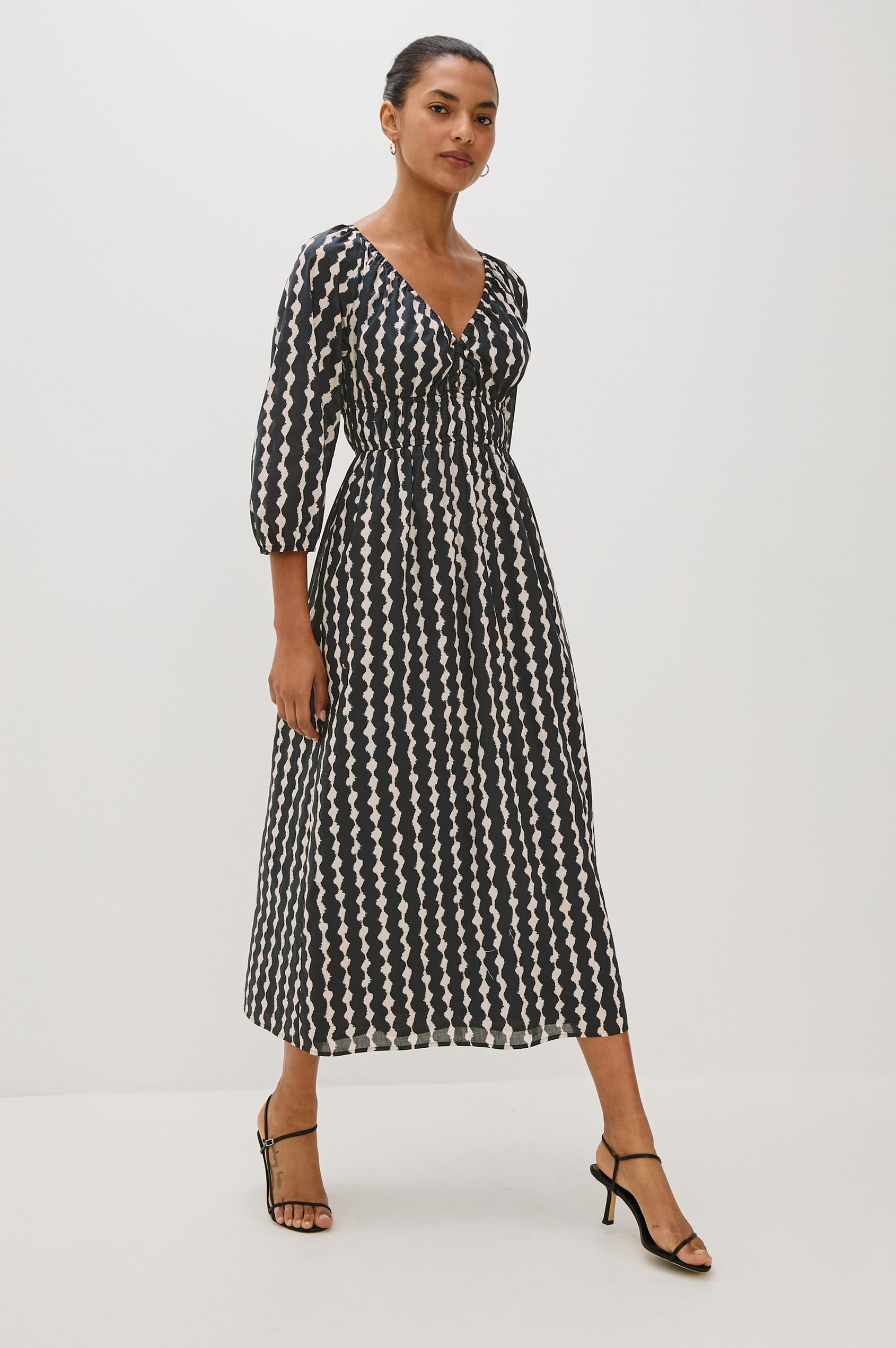Paio midi dress with a fitted bodice, three quarter sleeves with a slight puff effect, flowing skirt, and eyelet closures at the chest in Painted Noir colorway - full body front view of model in motion
