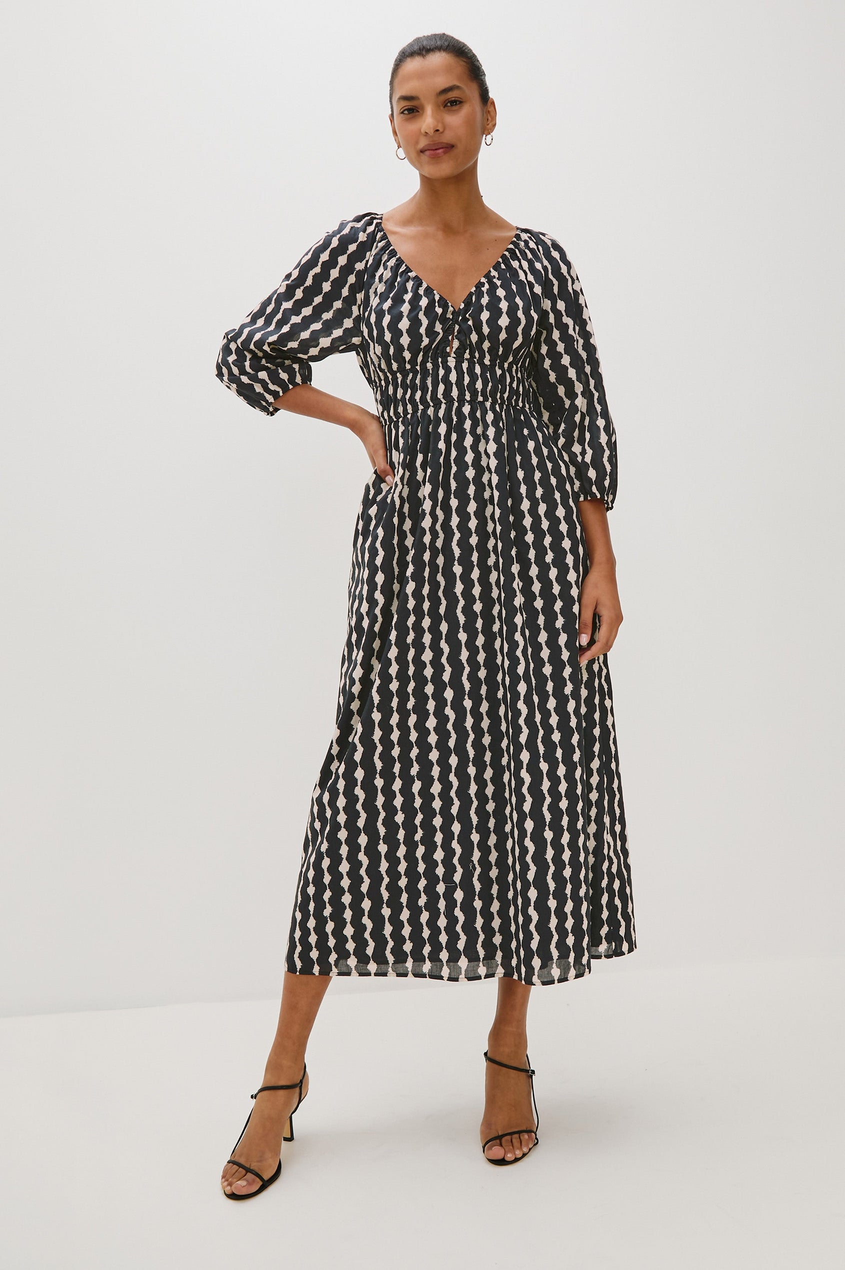 Paio midi dress with a fitted bodice, three quarter sleeves with a slight puff effect, flowing skirt, and eyelet closures at the chest in Painted Noir colorway - full body front view on model