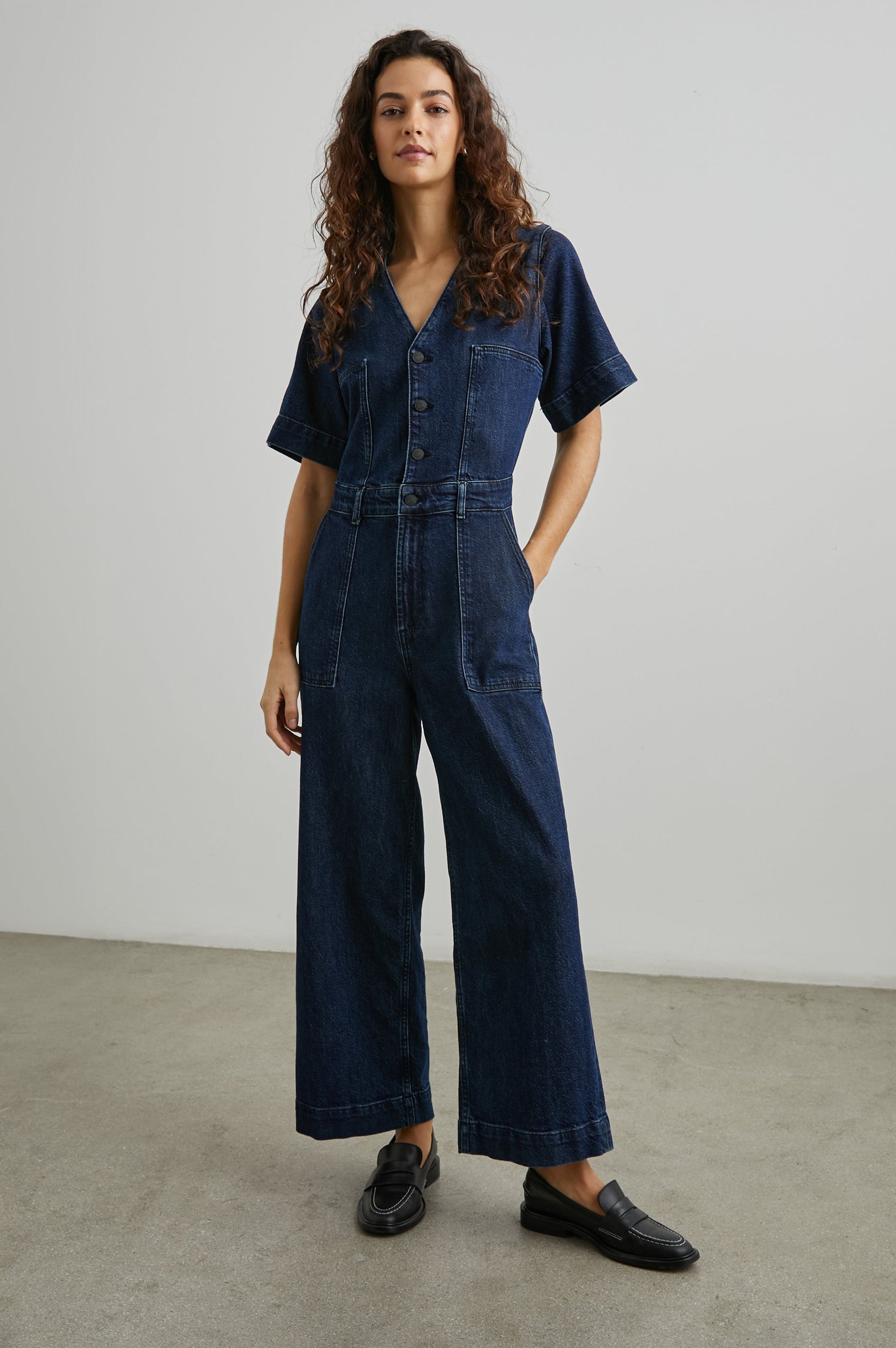 Palisades Short Sleeve Denim Jumpsuit with Wide Legs and Sleeves, Belt Loops, A Button and Zipper Closure for the Pants and Button Closure on the Bodice, a V neck, two Front Pockets and Two Back Patch Pockets in Blue Moon Colorway - Front Full Body View Featured on Model