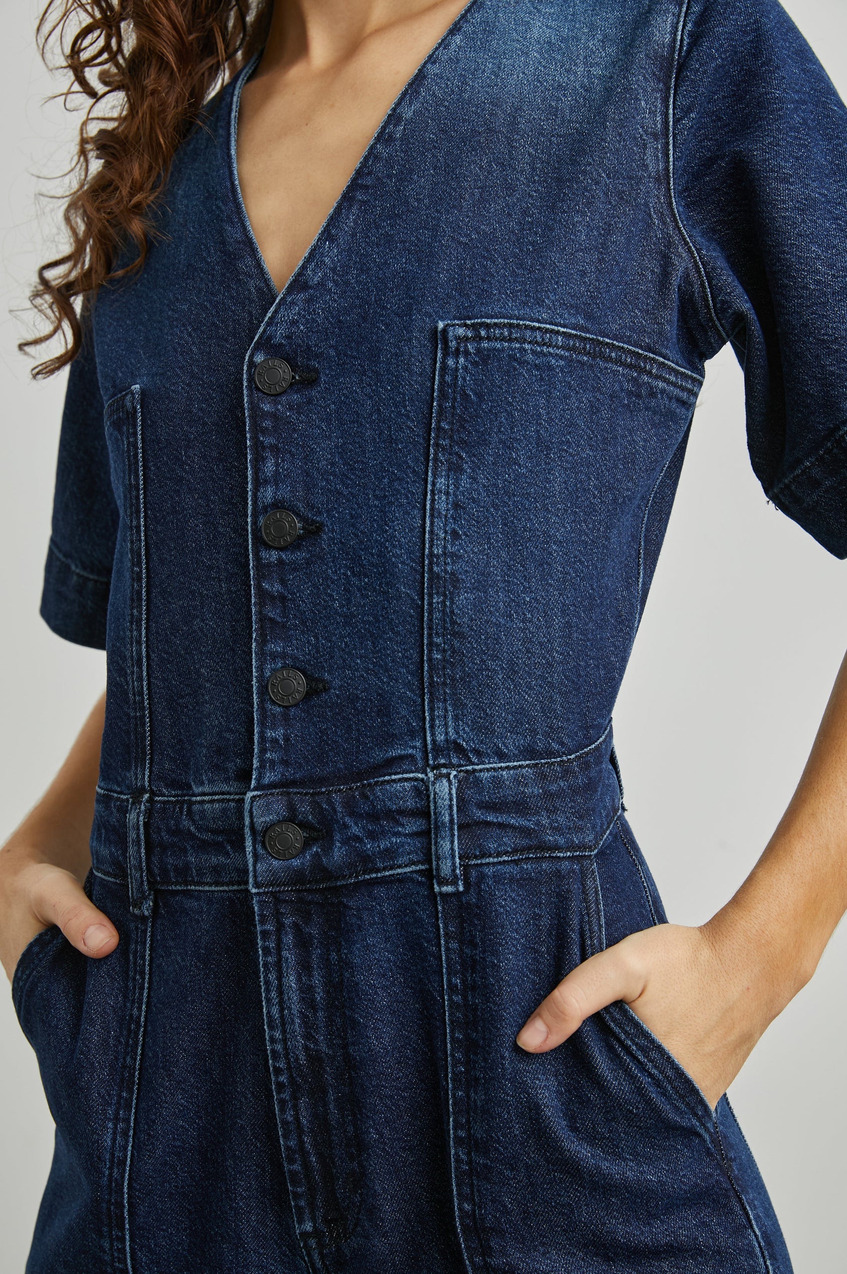 Palisades Short Sleeve Denim Jumpsuit with Wide Legs and Sleeves, Belt Loops, A Button and Zipper Closure for the Pants and Button Closure on the Bodice, a V neck, two Front Pockets and Two Back Patch Pockets in Blue Moon Colorway - Front View Featured on Model