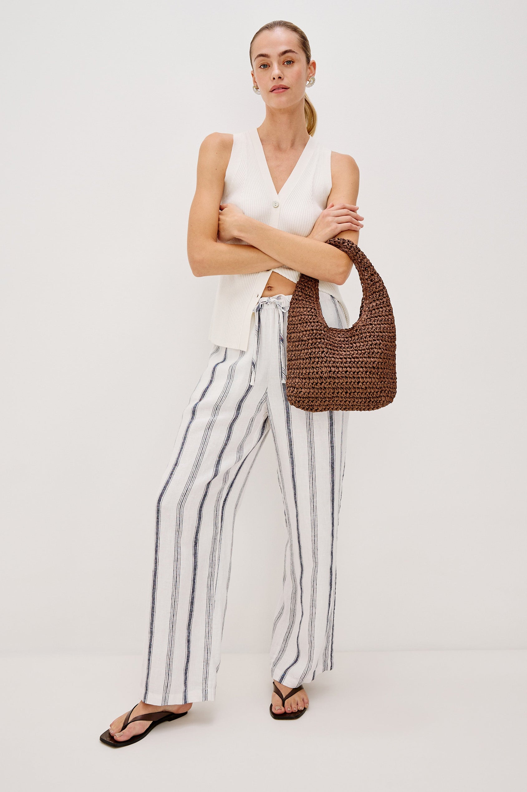 Palma Rattan Shoulder Bag with a Snap Closure and an Interior Pocket in Dark Brown Colorway. Front View of Model with Bag hanging on Elbow.