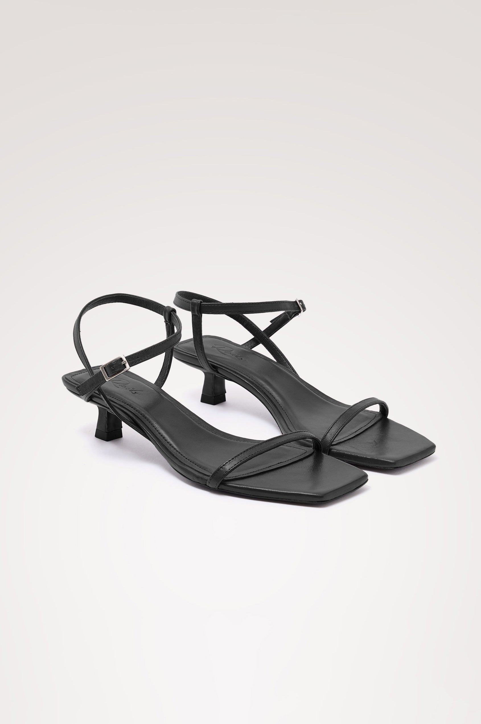 Palma Sandal Heel in Top-Grain Leather With Single Toe Strap, Adjustable Buckled Wrap Ankle Strap, and Low Heel in Black Colorway - angeled frontview of shoe.