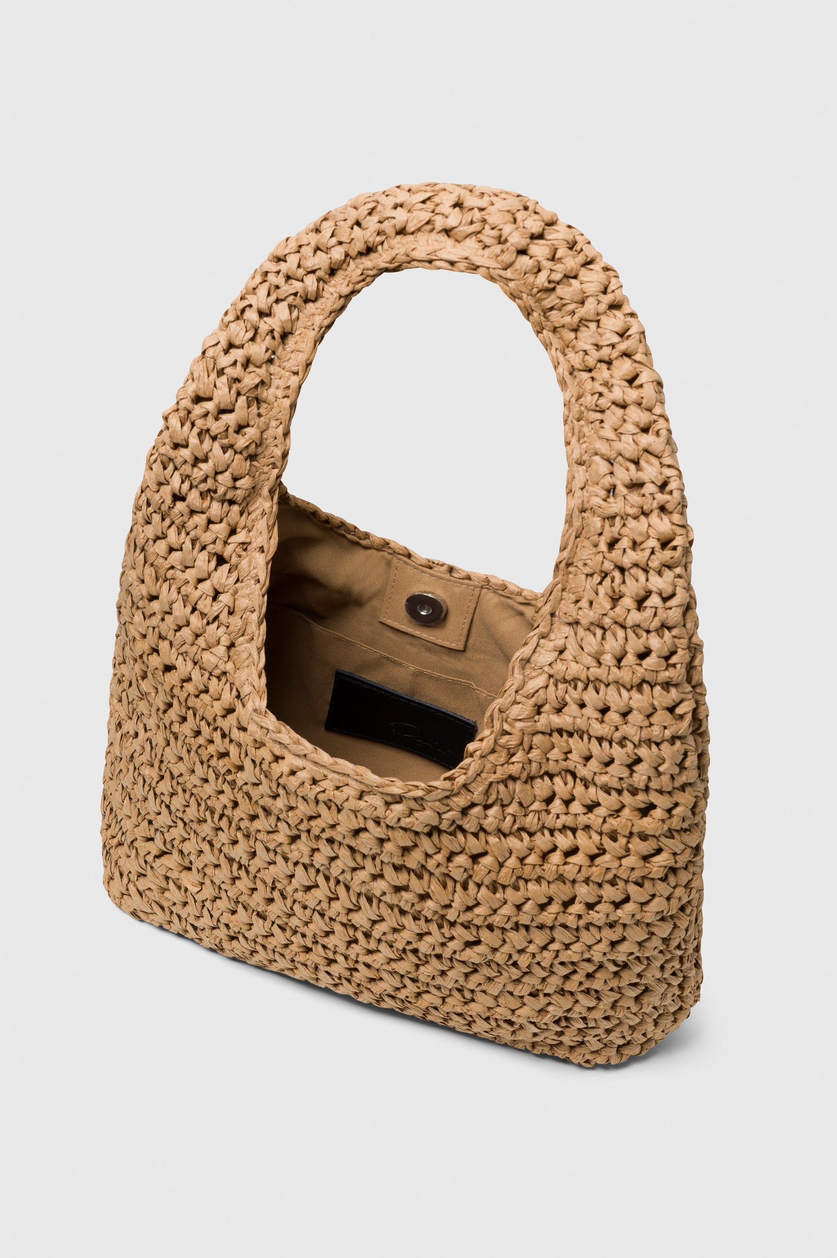Palma Rattan Shoulder Bag with a Snap Closure and an Interior Pocket in Tan Colorway. View of Bag Interior with Button Closure.