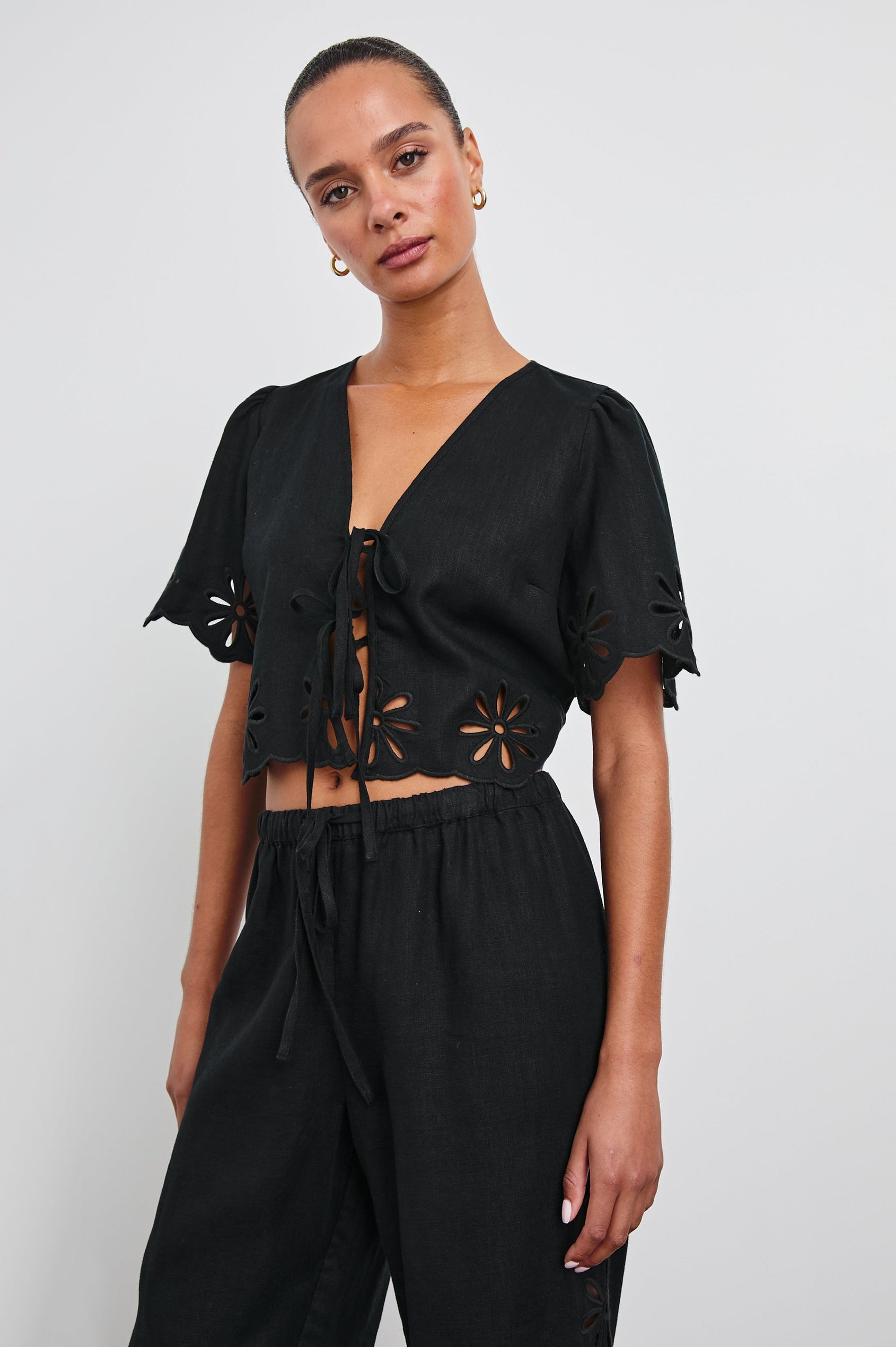 Pari Short-Sleeve Cropped Top with V Neck, Front Tie Closures, and Floral Eyelets in Black Eyelet Colorway - Front View Featured on Model 