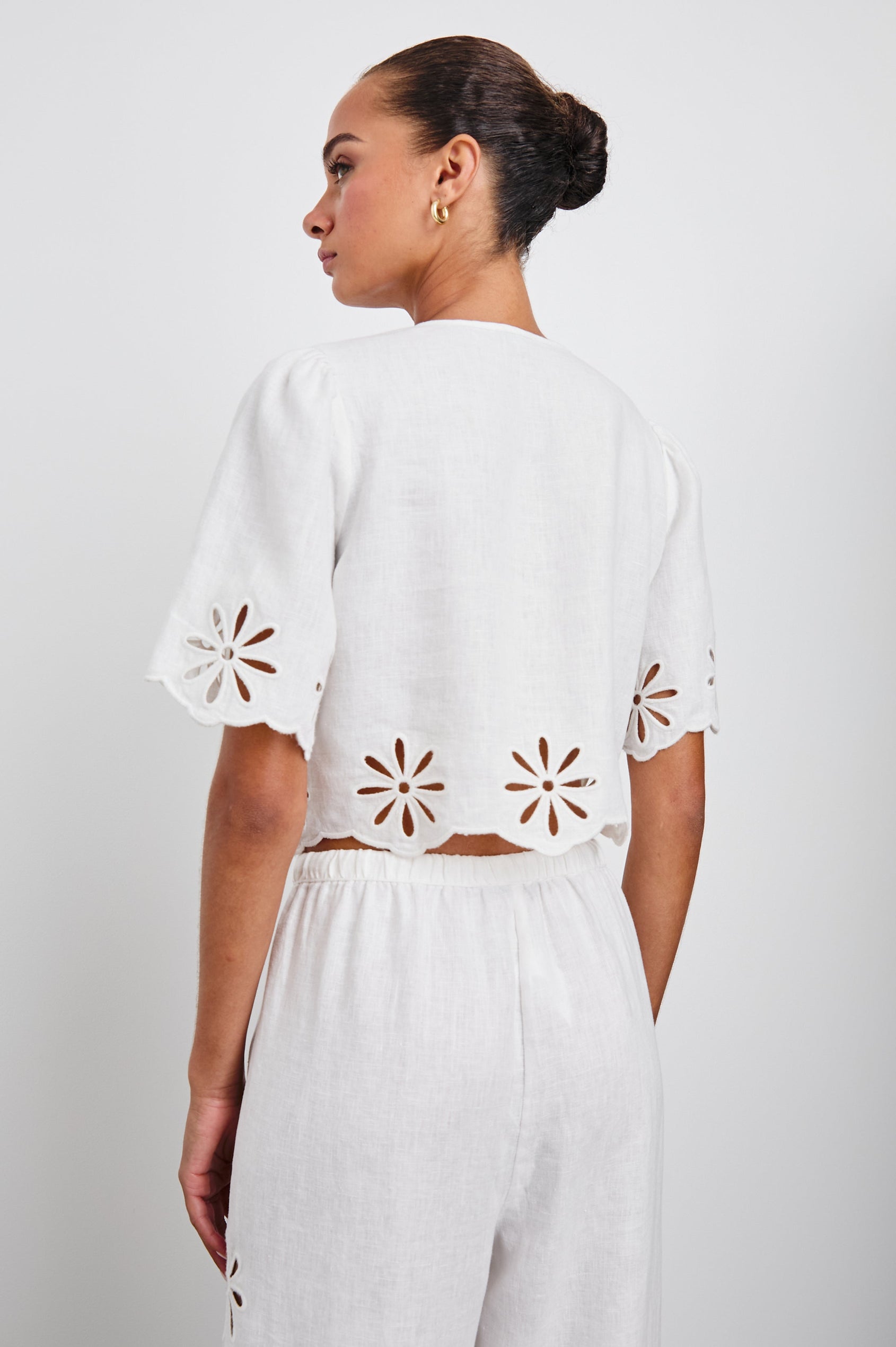 Pari Short-Sleeve Cropped Top with V Neck, Front Tie Closures, and Floral Eyelets in White Eyelet Colorway - Back View Featured on Model 