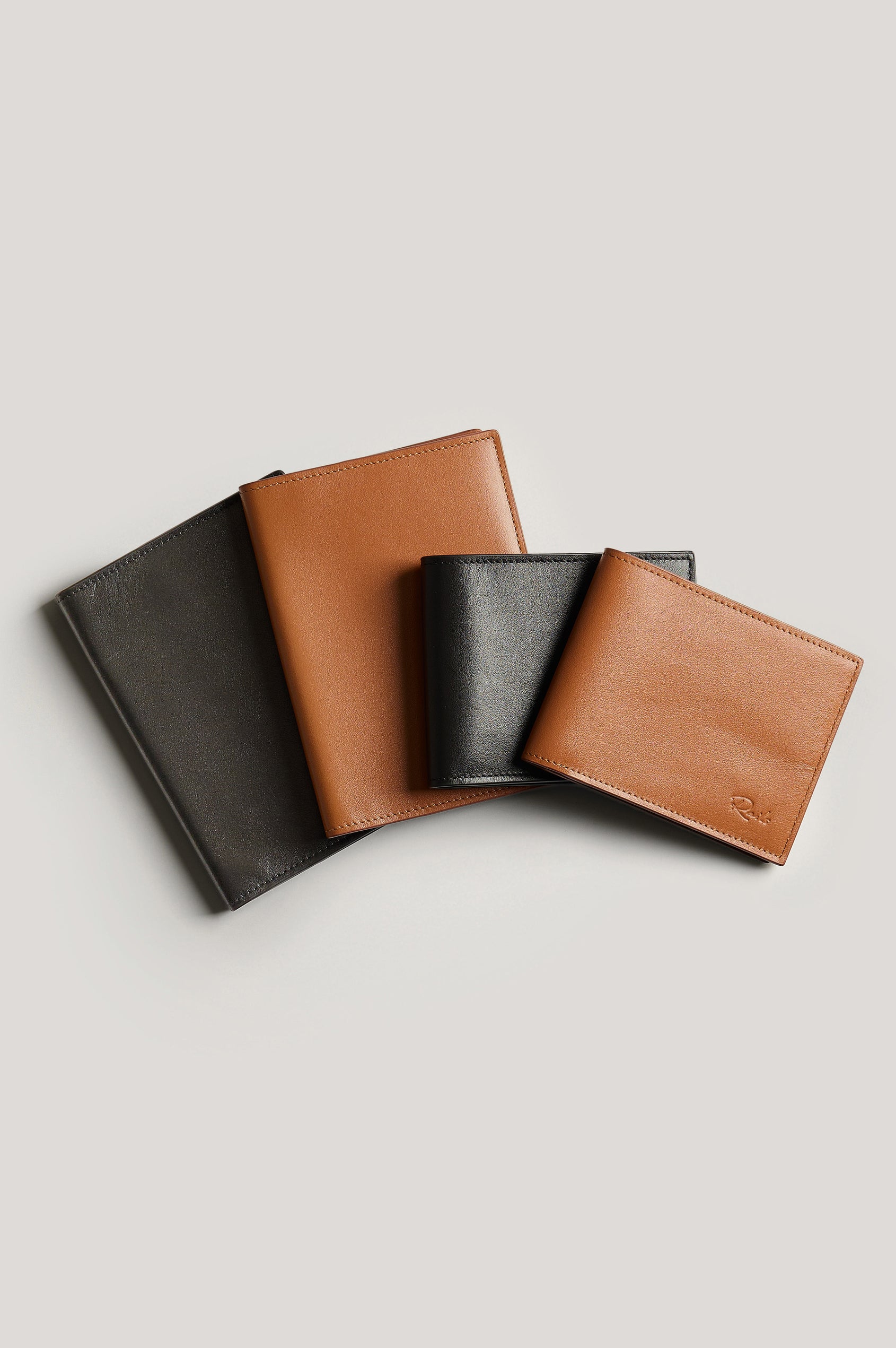 Leather passport holder folded, front view next to wallets for size reference.
