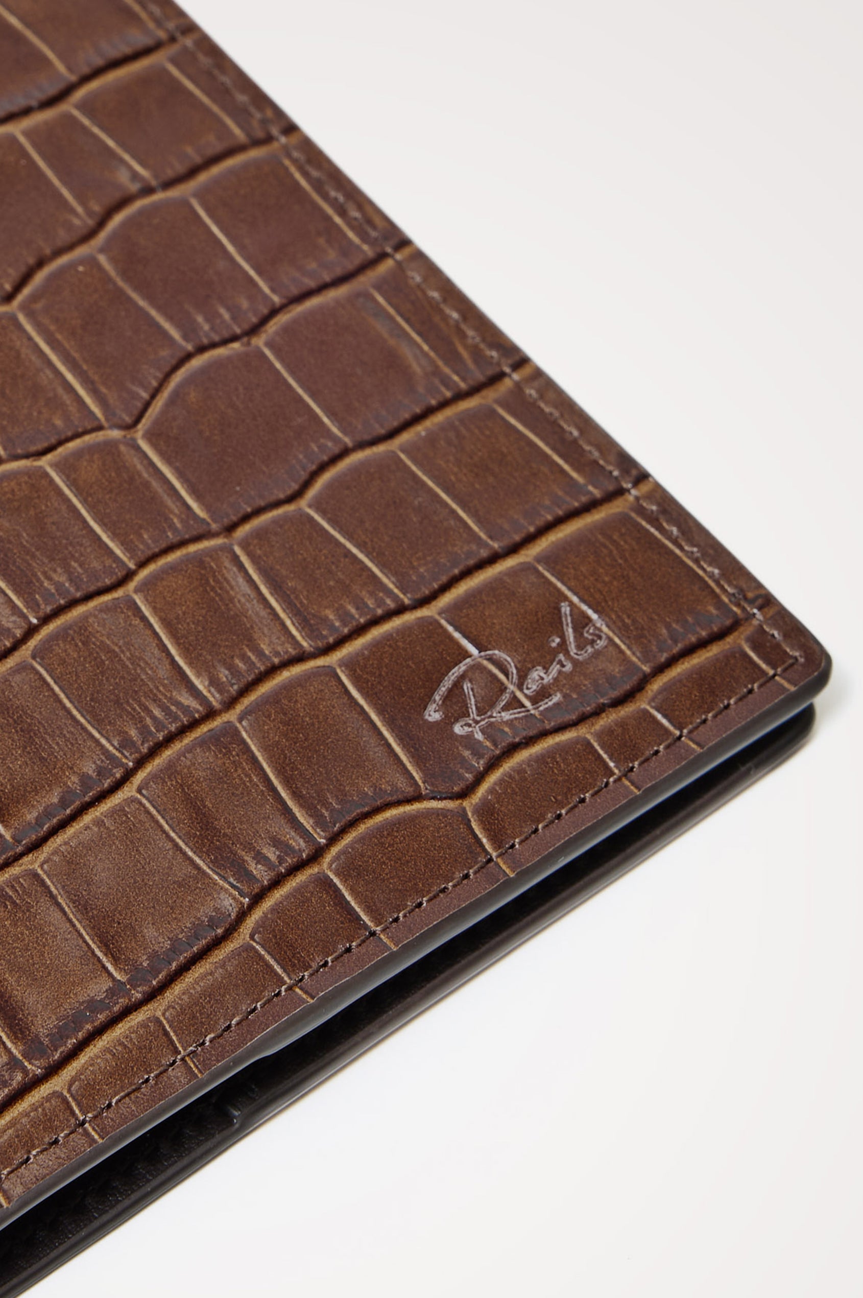 Passport Holder in Croc-Embossed Spanish Leather With Five Card Slots, Two Side Pockets, and Embossed Rails Logo in Dark Brown Croc Embossed Colorway - Front close-up flatlay view featured.