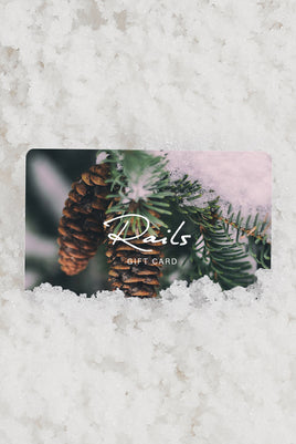 A rectangular Rail's gift card featuring pine branches, pinecones, and soft pink snow, placed on a textured white surface resembling snow.