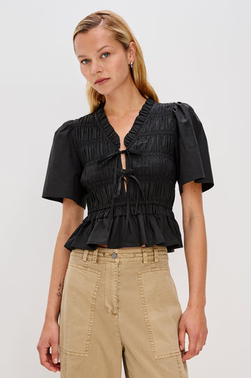 Portia V-Neck Tie Front Top with Short Puff Sleeves and a Ruffled Peplum Hem in Black Colorway. Front View Shown on Model.