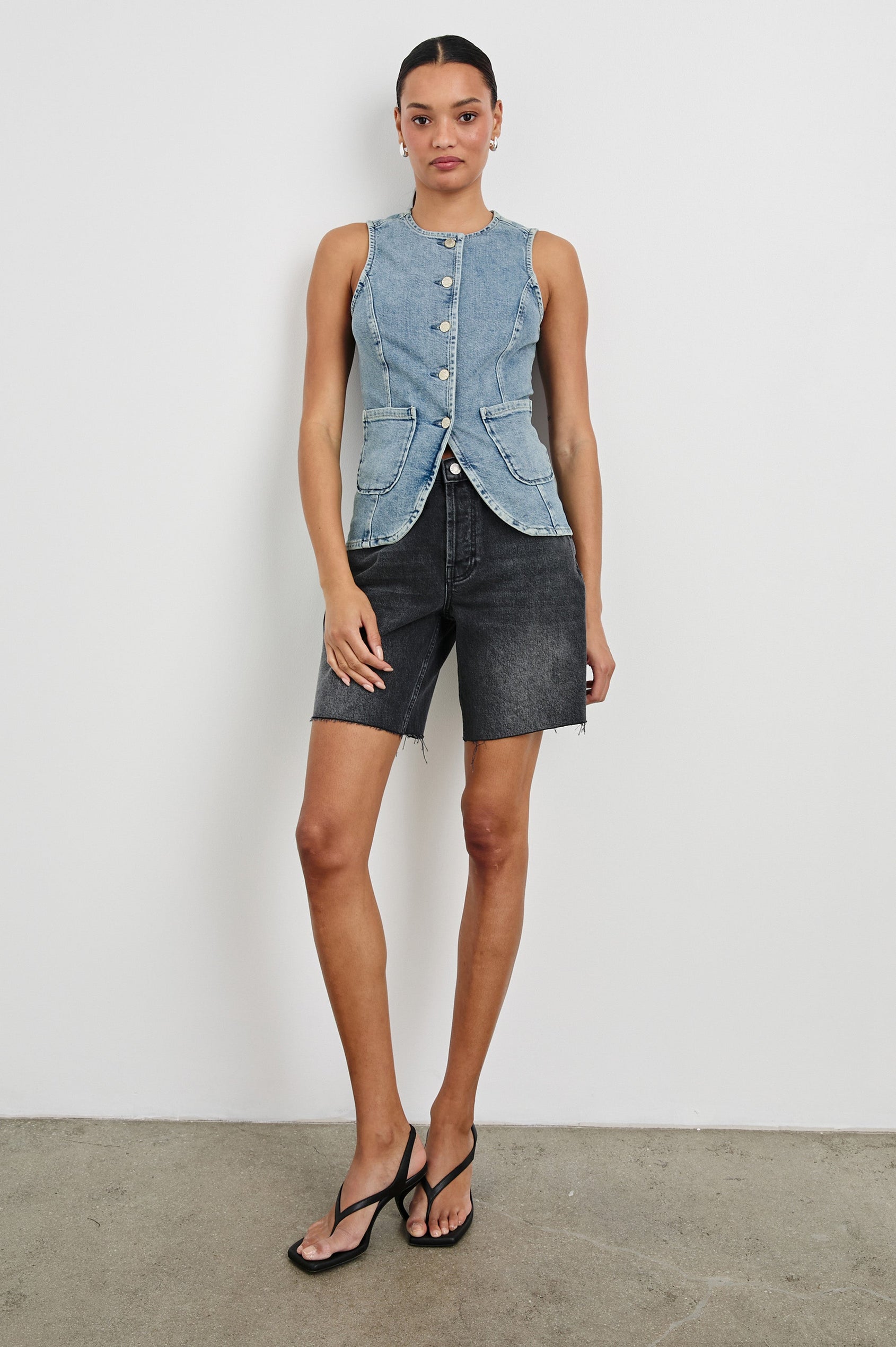 Portola Sleeveless Denim Vest with Exposed Button Front Closure, Crew Neck, Front Patch Pockets and a Scalloped Split Hem in Blue Eyed Girl Colorway. Full Body Front View Shown on Model.