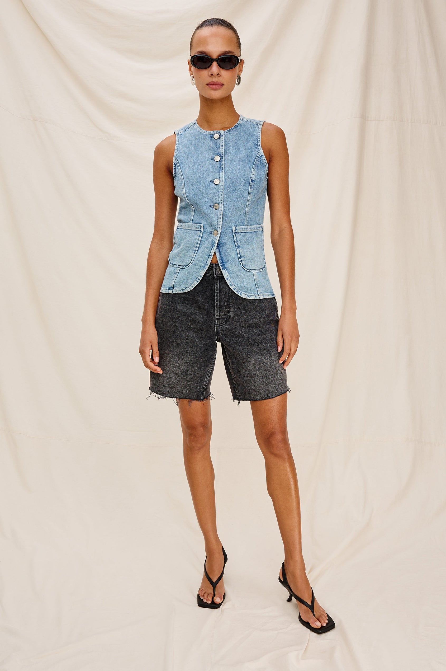Portola Sleeveless Denim Vest with Exposed Button Front Closure, Crew Neck, Front Patch Pockets and a Scalloped Split Hem in Blue Eyed Girl Colorway. Full Body Front View Shown on Model.