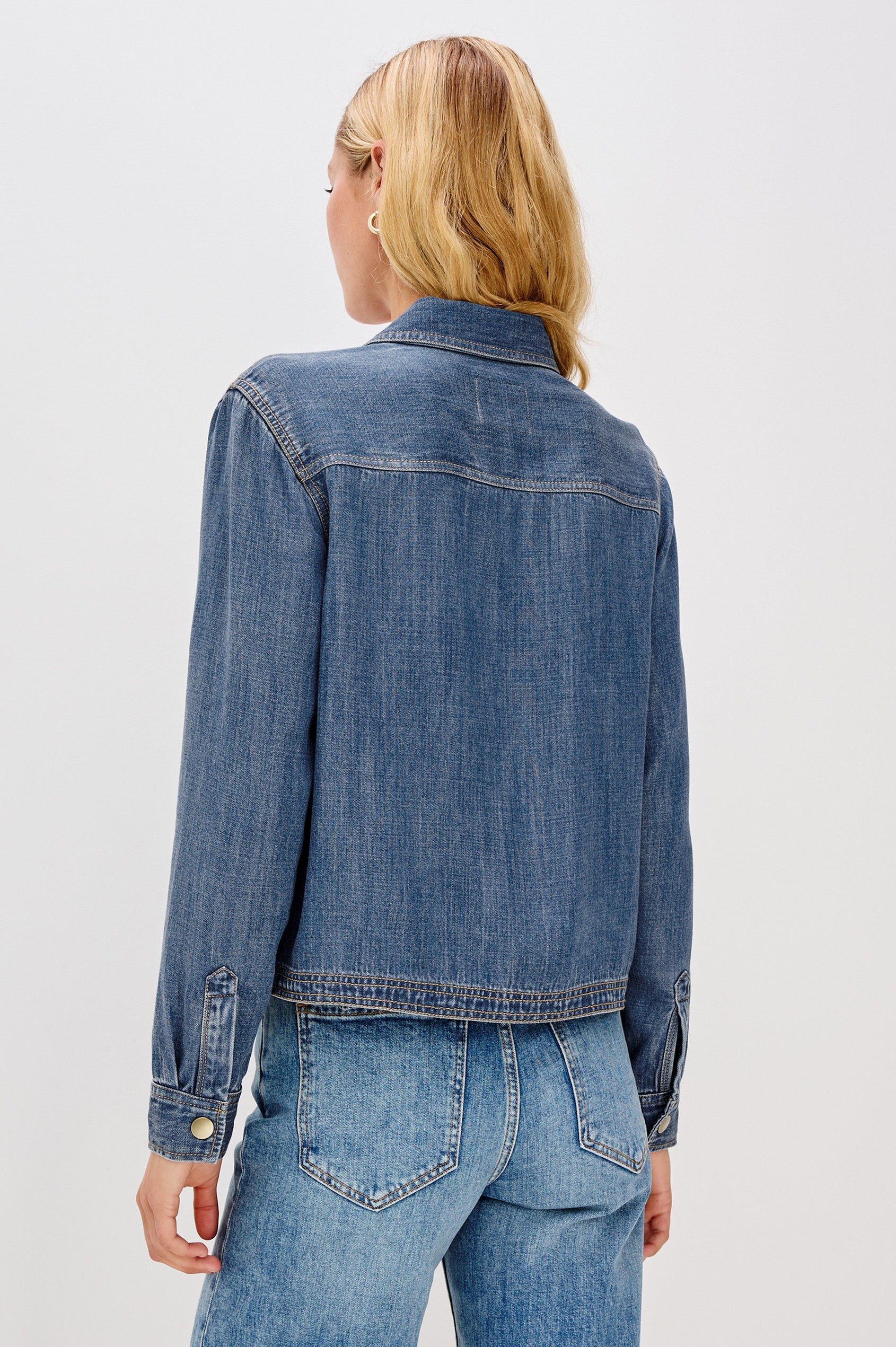 Ports is a soft, lightweight denim shirt with a cropped fit. The shirt features a half placket with snap-front closures, short sleeves, and two chest pockets in Antique Blue Colorway - Back View Featured on Model