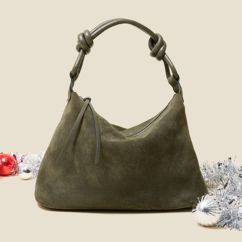 An olive green suede hobo handbag with a knotted leather handle, styled with silver tinsel and holiday ornaments on a light beige background.