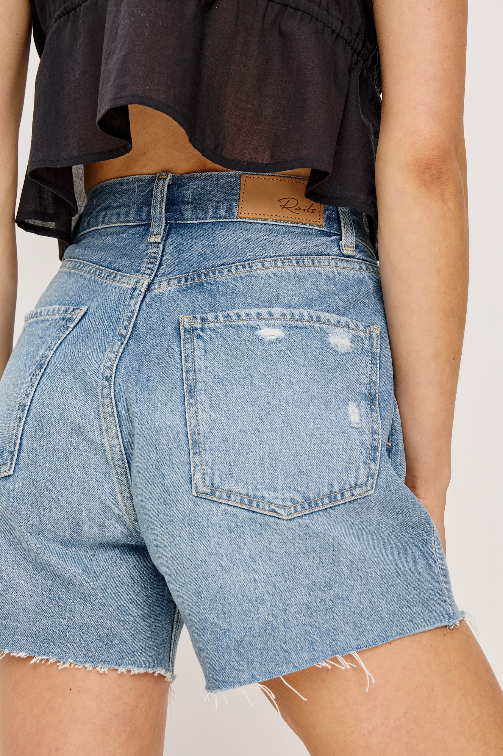 Rancho High-Waisted Short in Recycled Cotton Blend Denim With Light Stretch, Pinched Waist, Distressed Hem, A-Line SIlhouette, Relaxed Saddle, and Front Zip Fly in Crystal Cove Colorway - Lower Body Back View Featured on Model