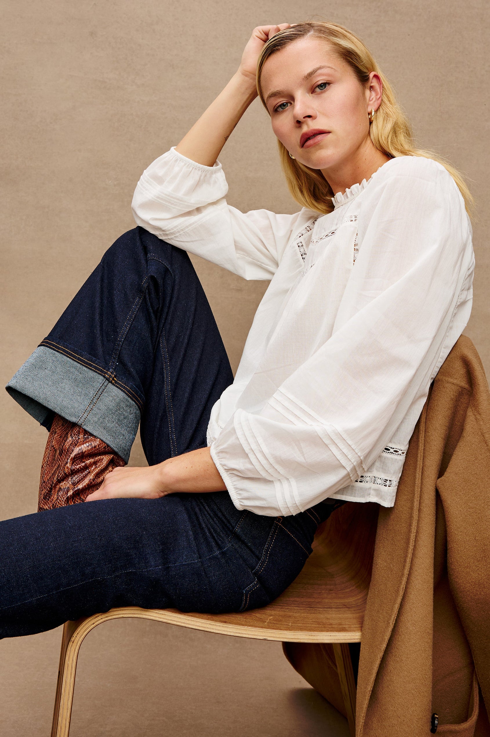 Stylized front view of female model wearing our Reyna Top in white. This is a long sleeve crewneck baby doll blouse, with ruffles at the collar. 