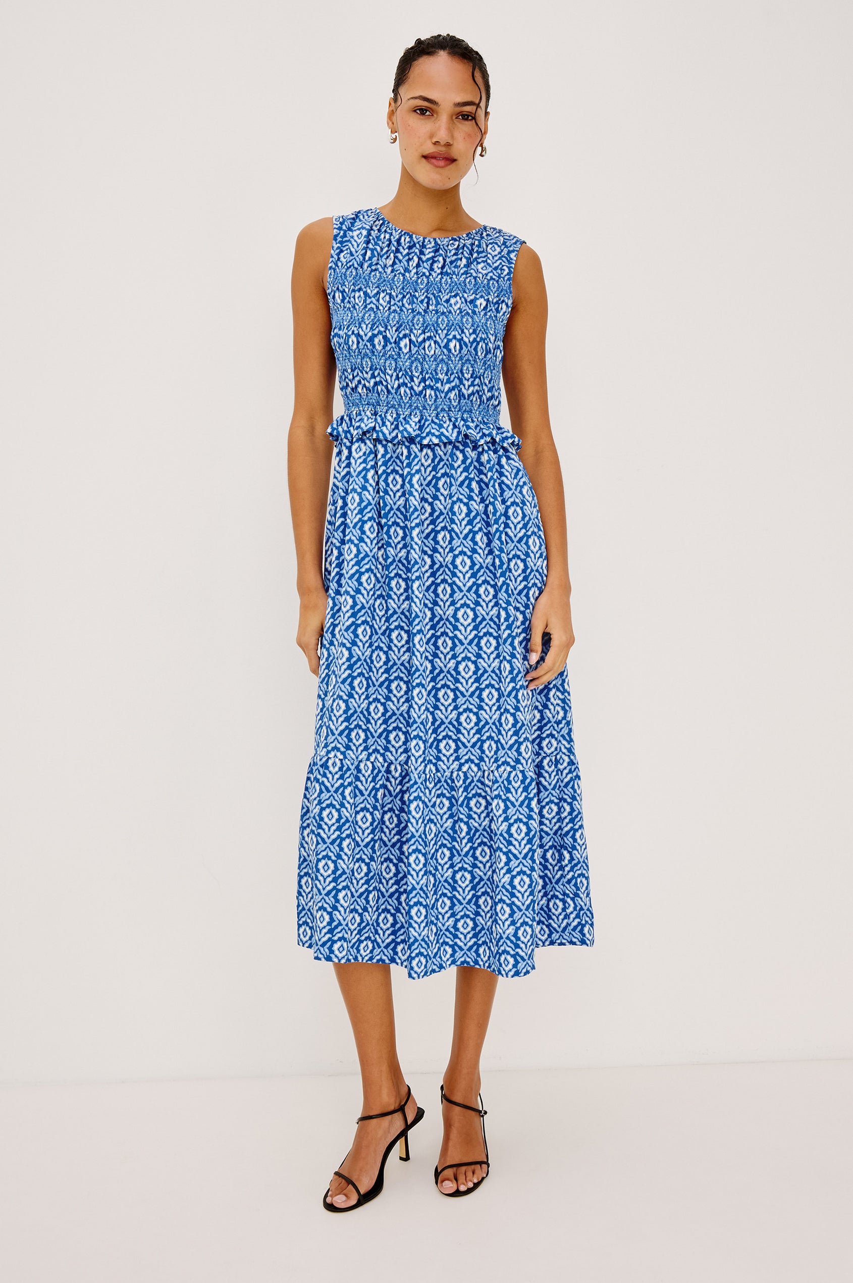 Rialto Midi Dress in Cotton Poplin With High Neckline, Smocked Bodice, Sleeveless Cut, Ruffle Trim, and Tiered Hem in Blue Ikat Colorway - Full Body Front View Featured on Model