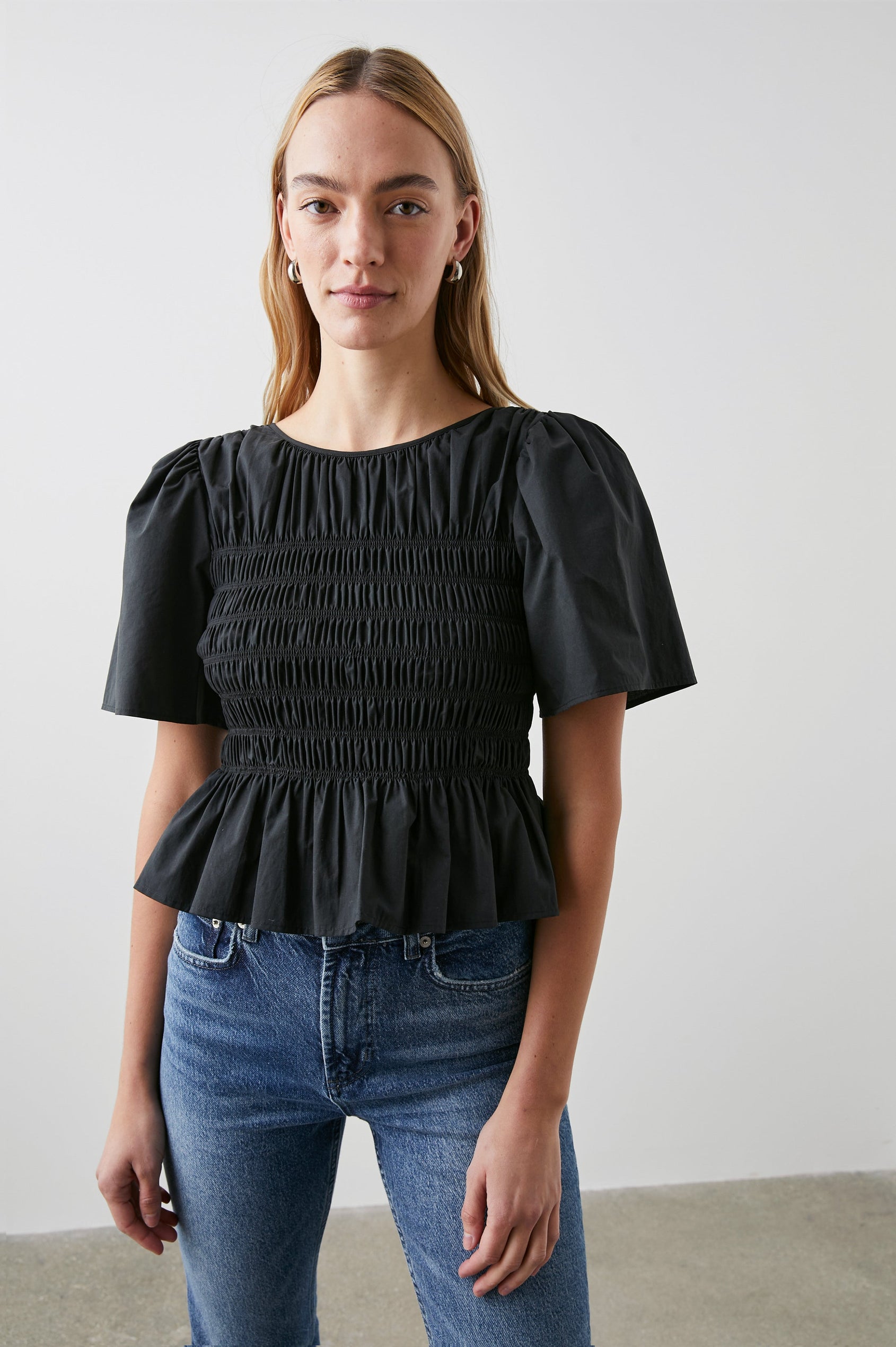 Rosie Short-Sleeve Top with a Smocked Center Bodice, Pleats at the Hem and Yoke and a Upper Back Tie Closure in Black Colorway - Front View Featured on Model