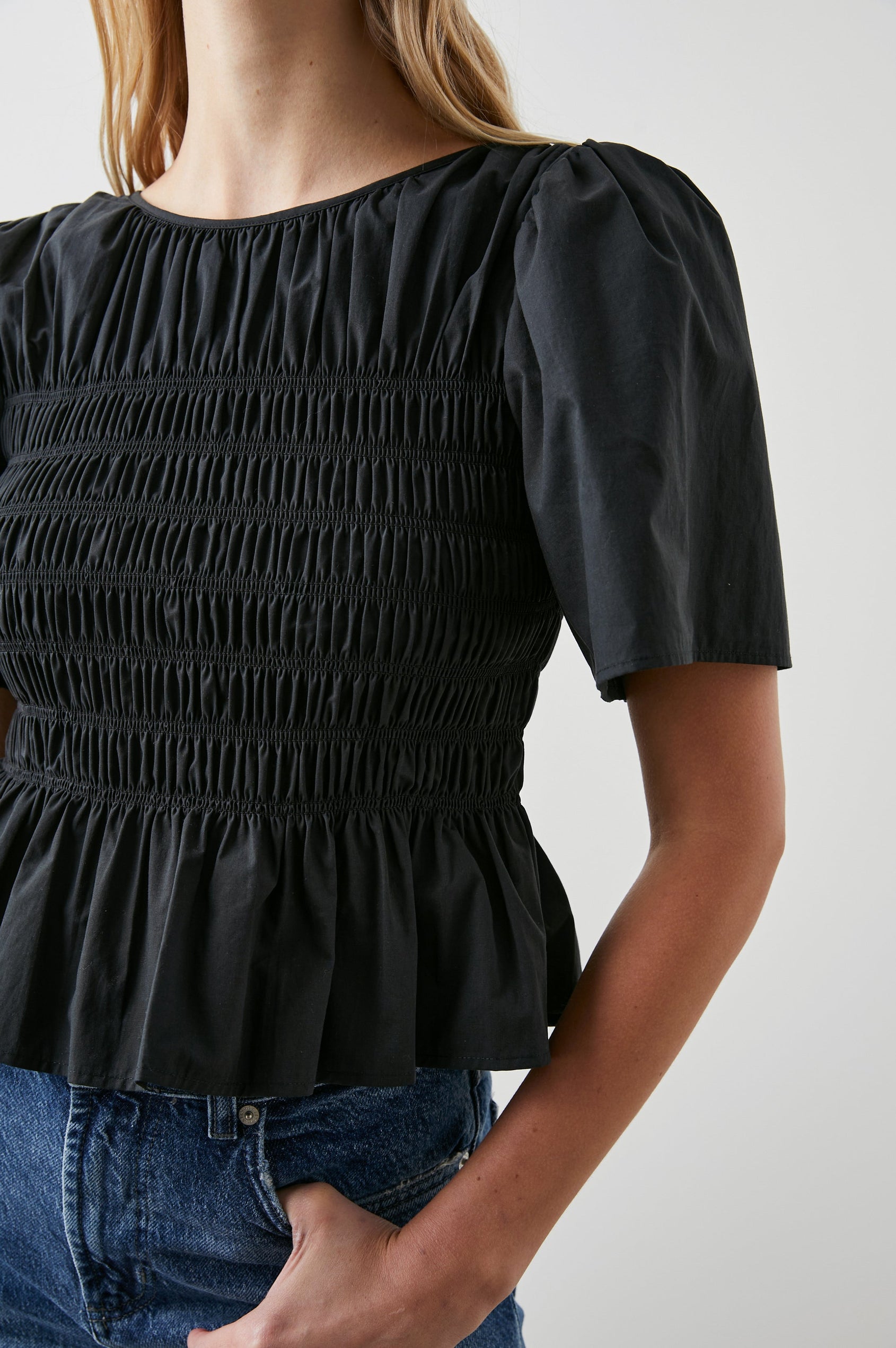 Rosie Short-Sleeve Top with a Smocked Center Bodice, Pleats at the Hem and Yoke and a Upper Back Tie Closure in Black Colorway - Front View Featured on Model