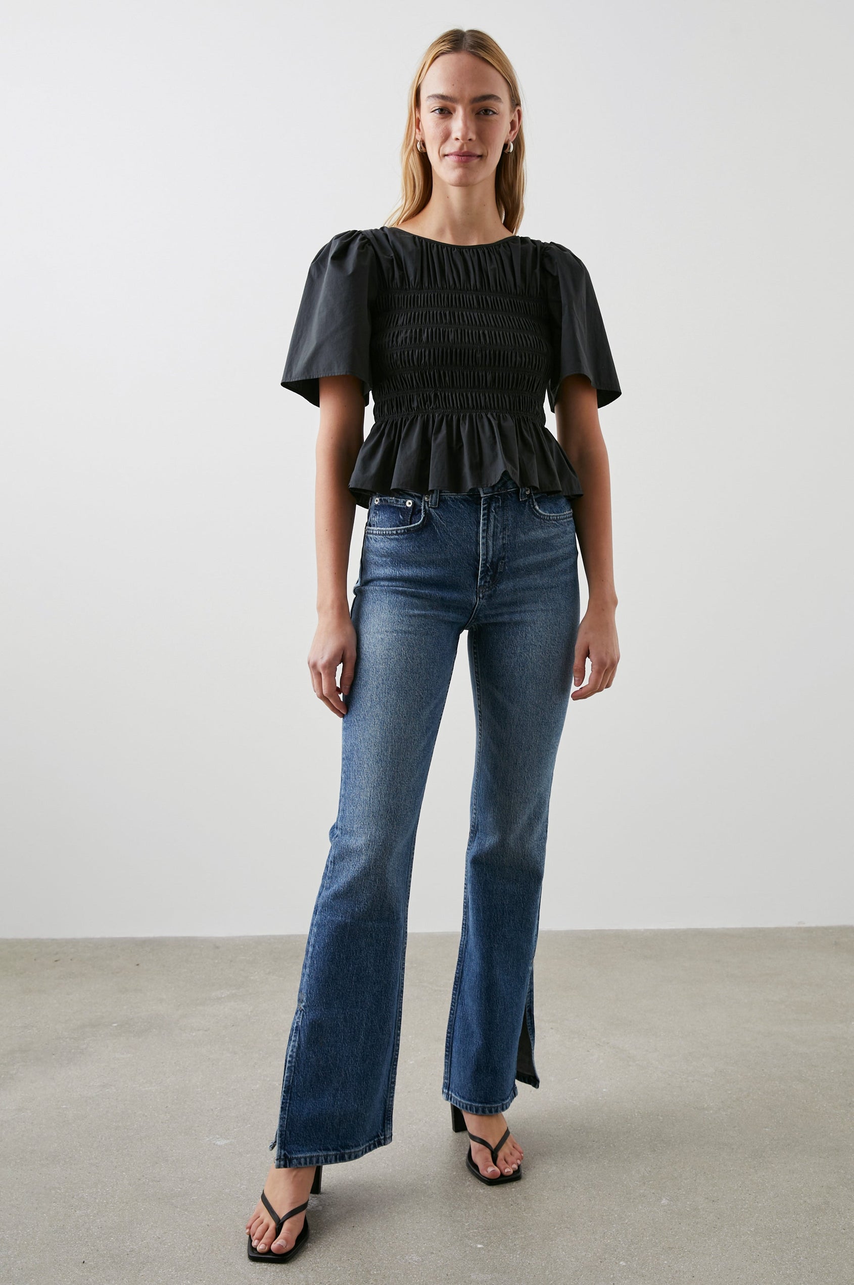Rosie Short-Sleeve Top with a Smocked Center Bodice, Pleats at the Hem and Yoke and a Upper Back Tie Closure in Black Colorway - Front Full Body View Featured on Model