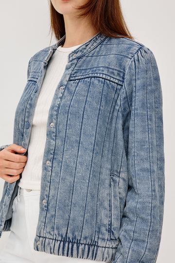 The Rosell is a boxy bomber jacket in ultra-soft quilted washed denim with snap button closures, elastic cuffs and hem, and long puff sleeves. Front detail view featured on model.