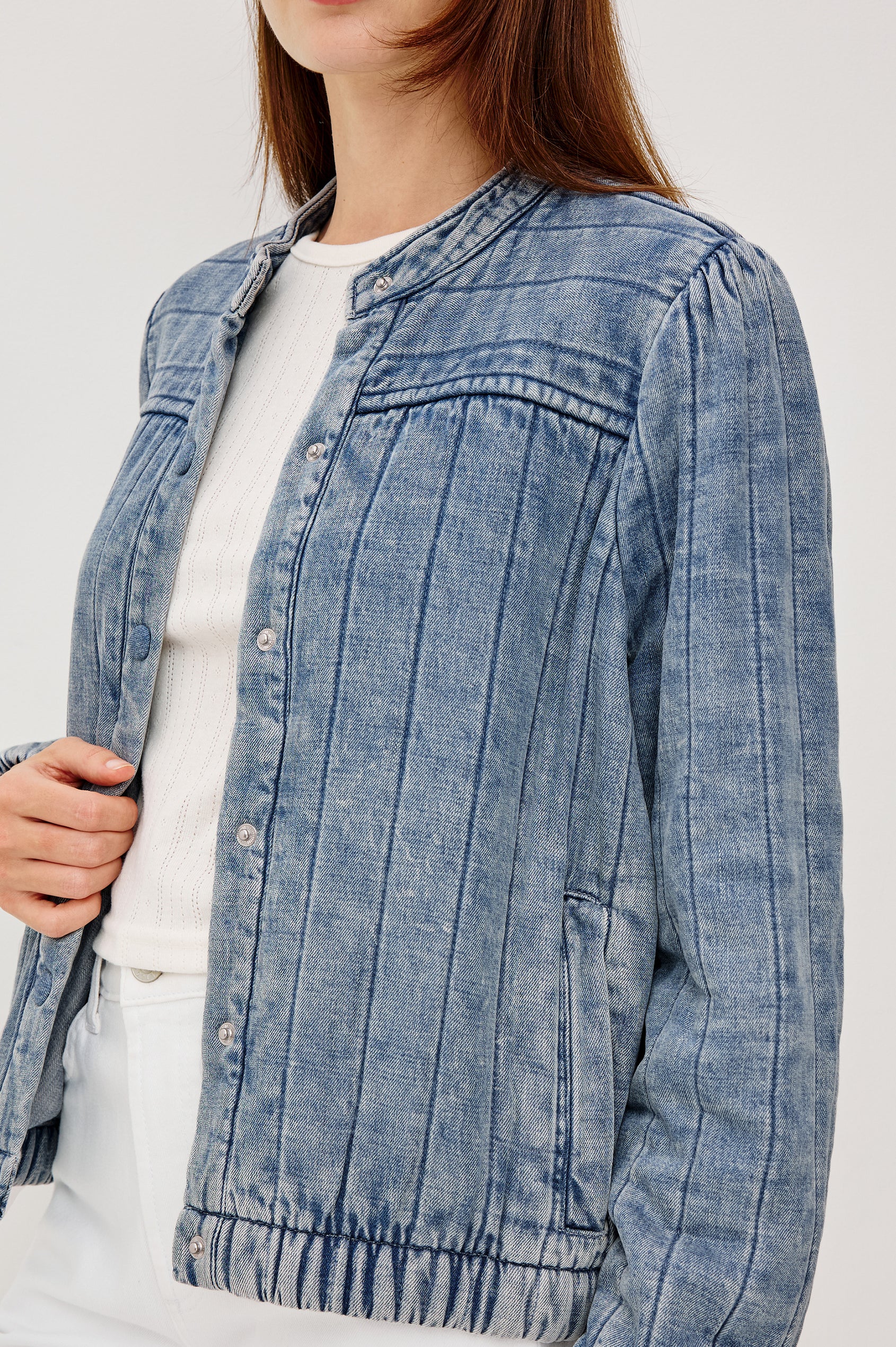 The Rosell is a boxy bomber jacket in ultra-soft quilted washed denim with snap button closures, elastic cuffs and hem, and long puff sleeves. Front detail view featured on model.