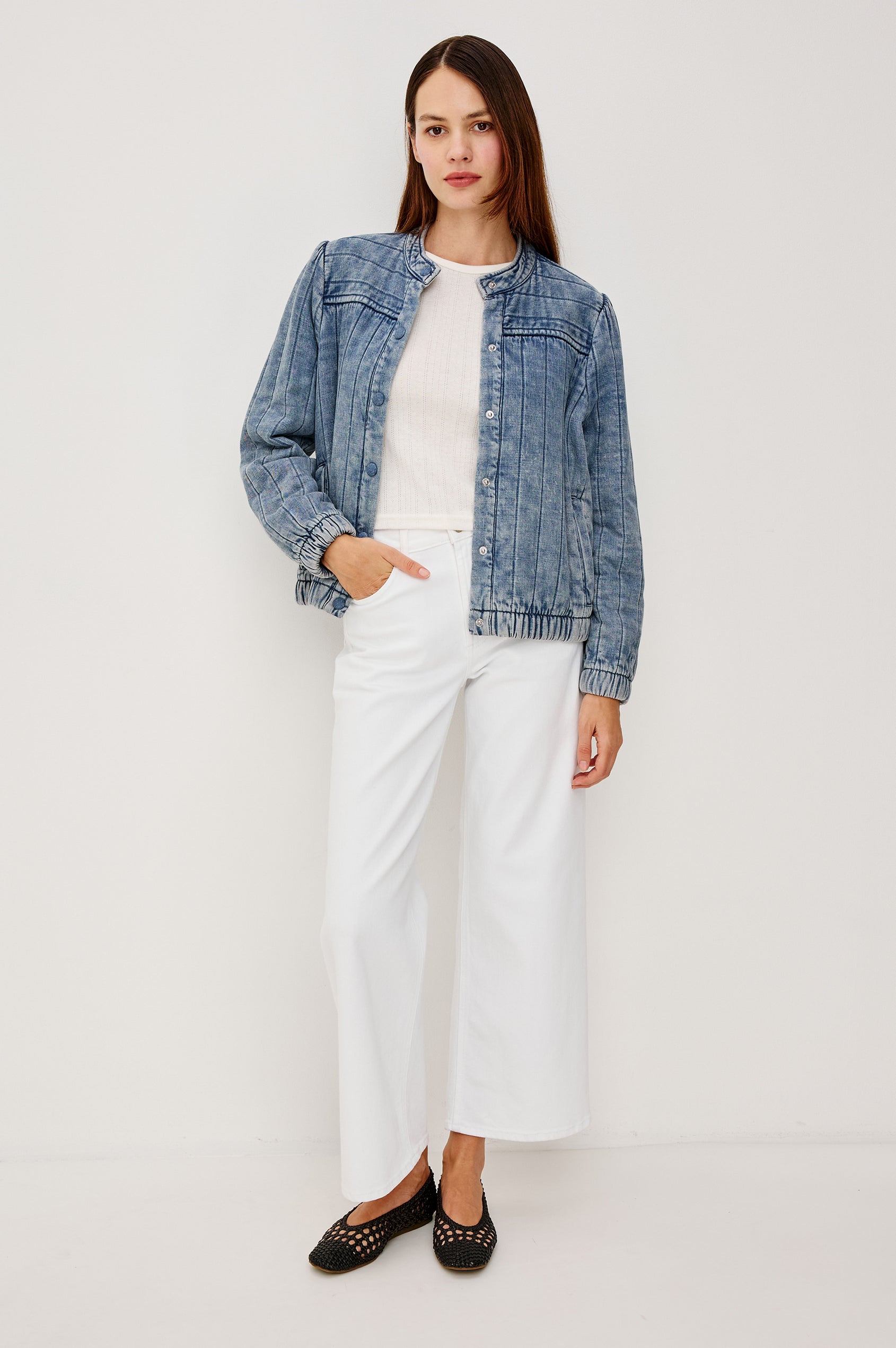 The Rosell is a boxy bomber jacket in ultra-soft quilted washed denim with snap button closures, elastic cuffs and hem, and long puff sleeves. Front full body view featured on model.