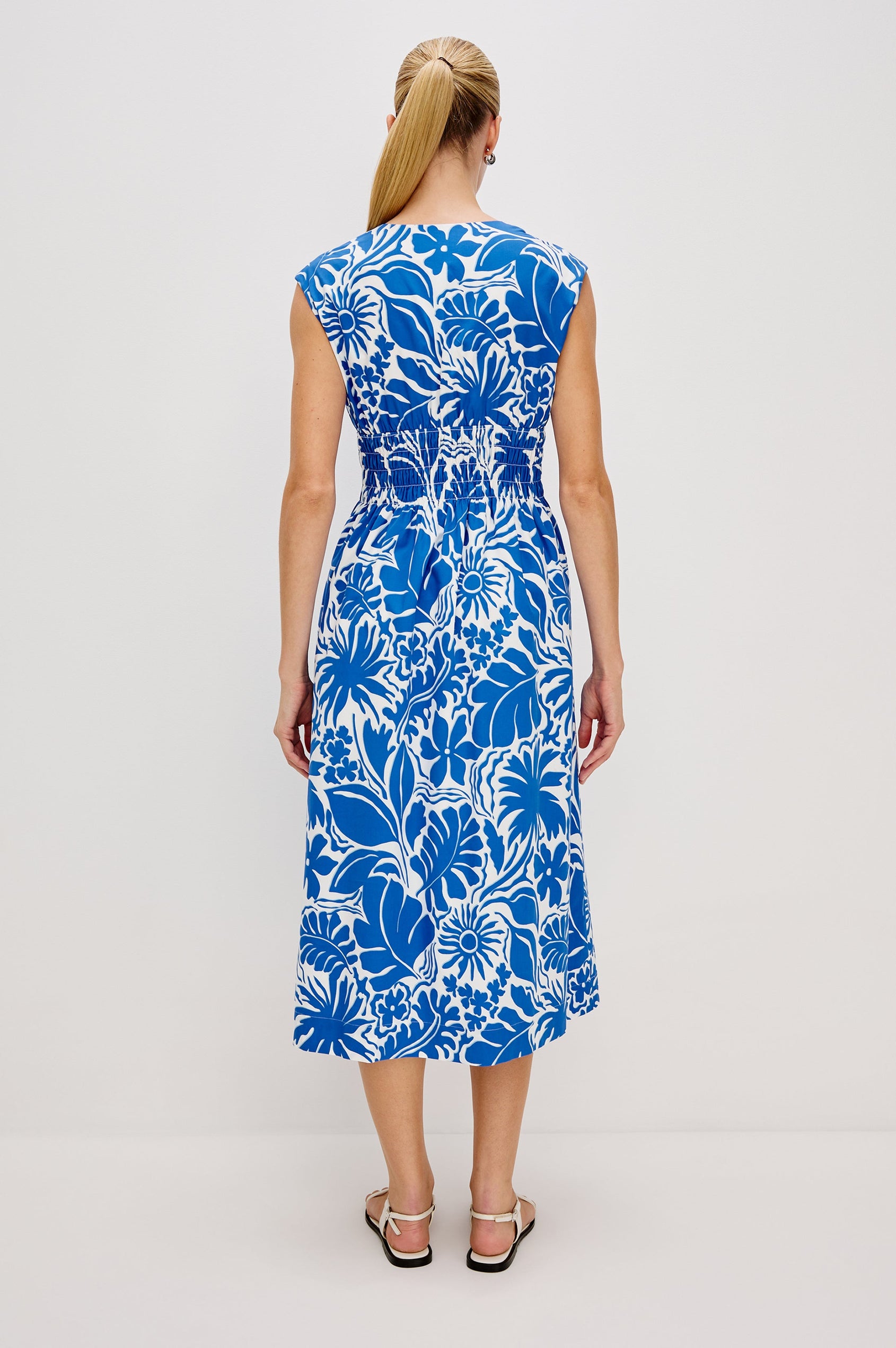 Roxanne A-Line Midi Dress with Smocked Waist, V-Neck, Cap Sleeve and Side Pockets in Blue Riviera Colorway. Full Body Back View Shown on Model.
