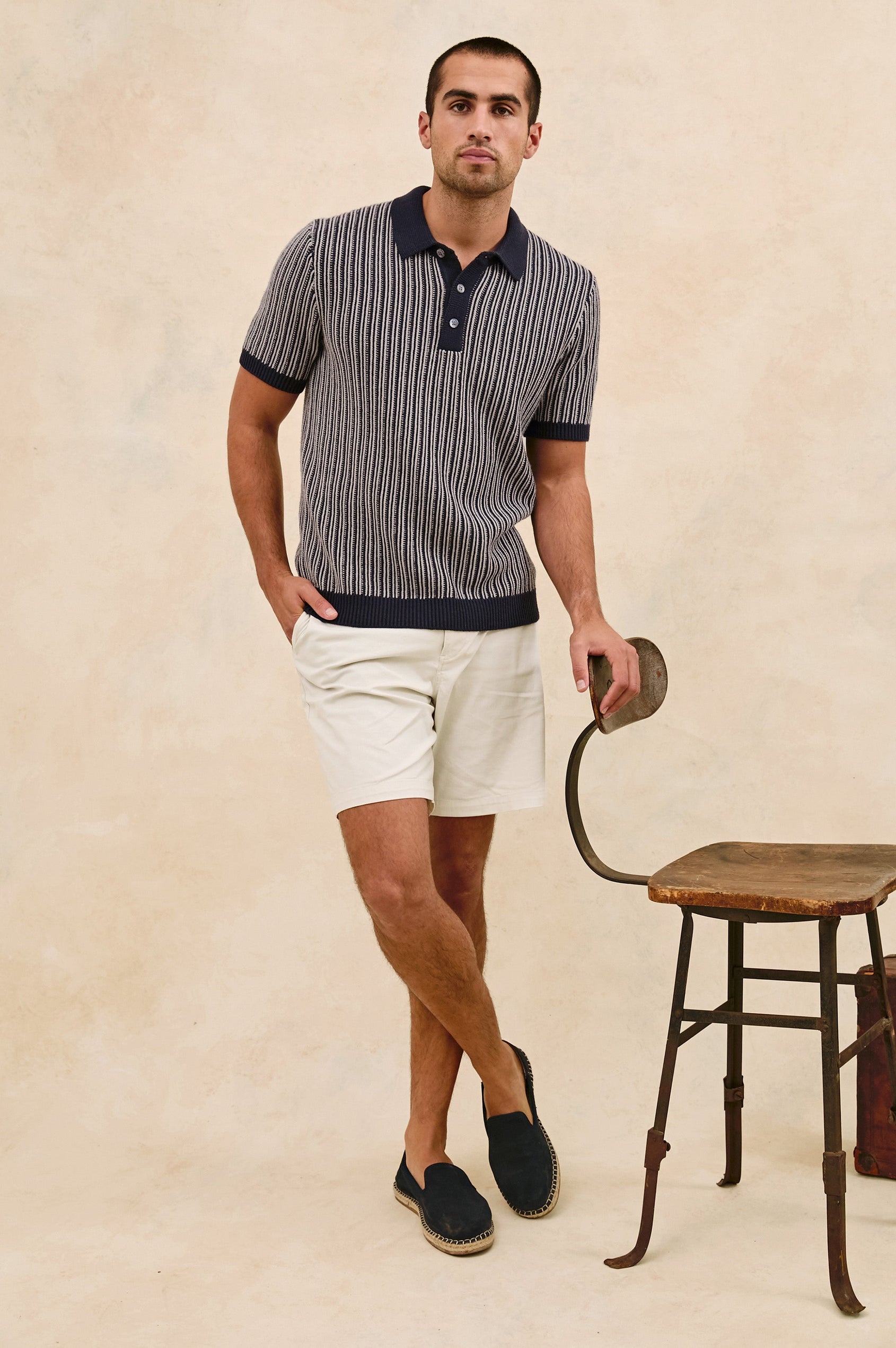 Royce ribbed knit short sleeve polo with three front buttons and a collar in Navy Grey - stylized full body front view on model, with chair