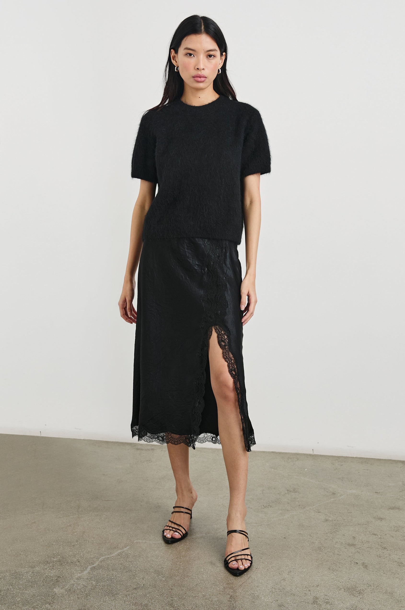 Rylan Midi Skirt with Front Thigh Slit and Trimmed with Scalloped Lace in Black Crinkle Colorway - Front Full Body View Featured on Model