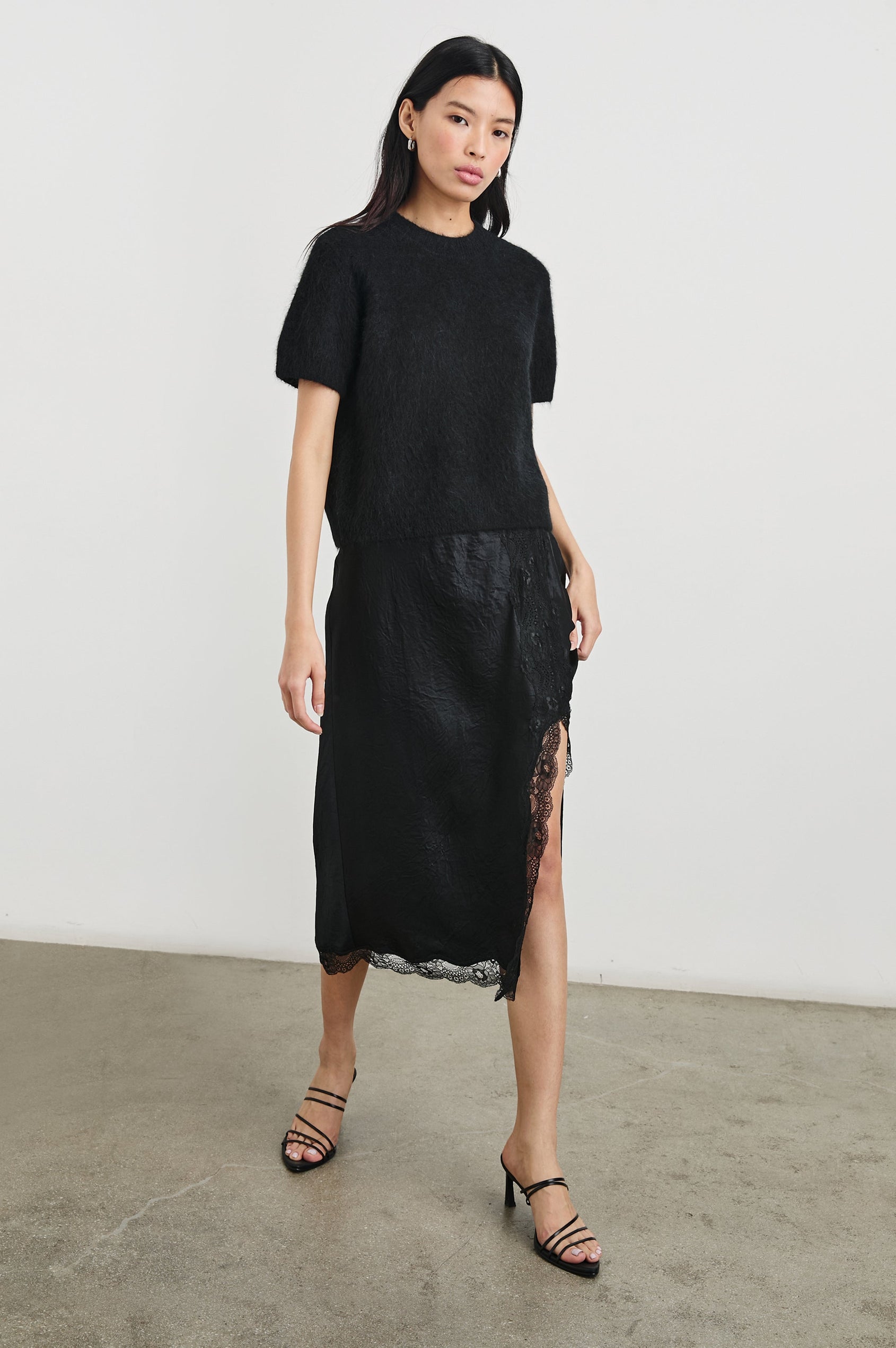 Rylan Midi Skirt with Front Thigh Slit and Trimmed with Scalloped Lace in Black Crinkle Colorway - Front Full Body View Featured on Model