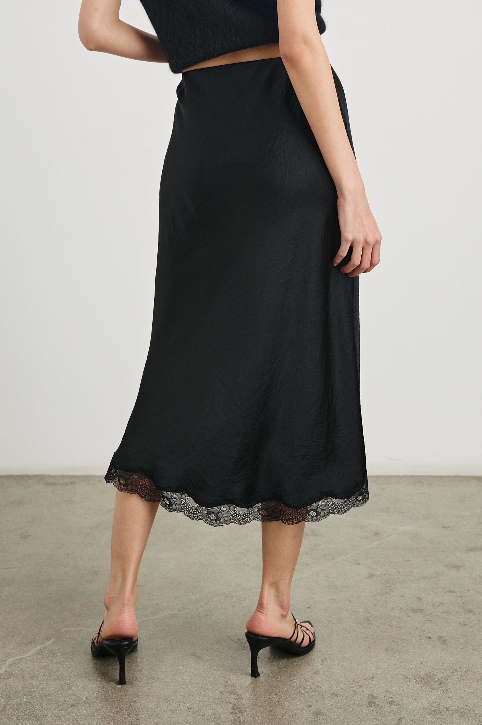 Rylan Midi Skirt with Front Thigh Slit and Trimmed with Scalloped Lace in Black Crinkle Colorway - Back View Featured on Model