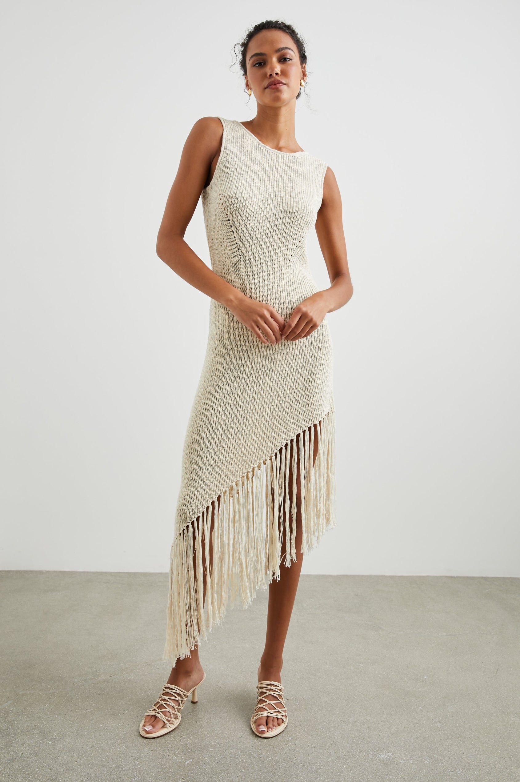 Rylee Sleeveless Ribbed Dress with a Scoop Neck, and a Fringed Asymmetrical Hemline from the Upper Thigh to the Knee in Ecru Colorway - Front Full Body View Featured on Model