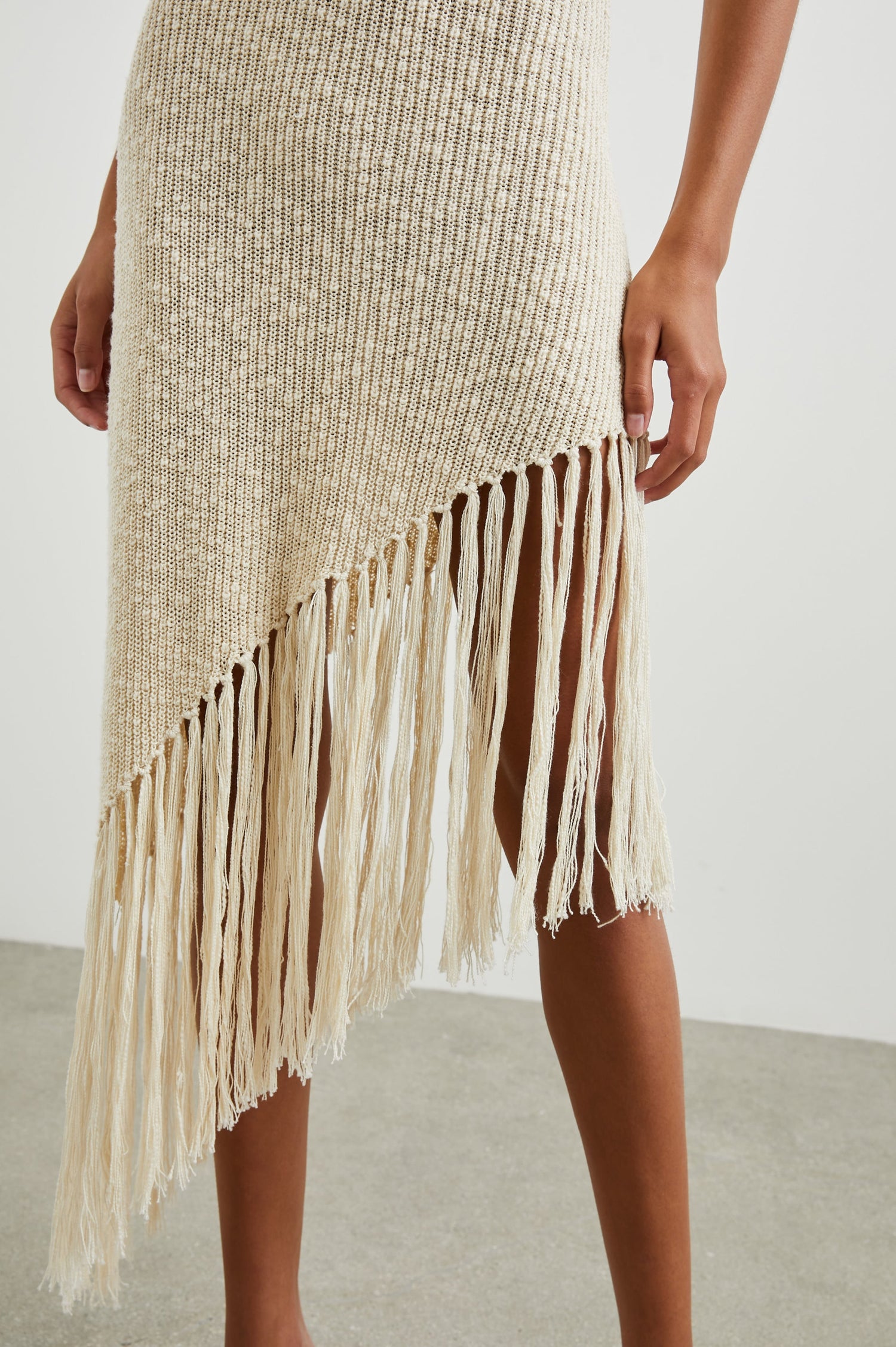 Rylee Sleeveless Ribbed Dress with a Scoop Neck, and a Fringed Asymmetrical Hemline from the Upper Thigh to the Knee in Ecru Colorway - Front View Featured on Model