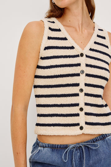 The Sade is a button front sweater vest with a v-neck in Ivory Navy Stripe colorway. Front detail view featured on model. 