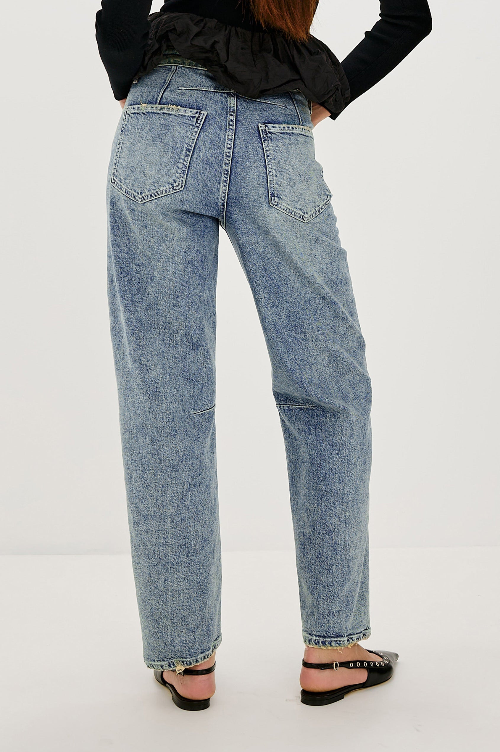 The Samo is a denim barrel leg jean, it features a low-slung fit in light-stretch denim with darting details and a subtle curved seam in Desert Sky wash, a vintage wash with yellow tint. Back view featured on model.